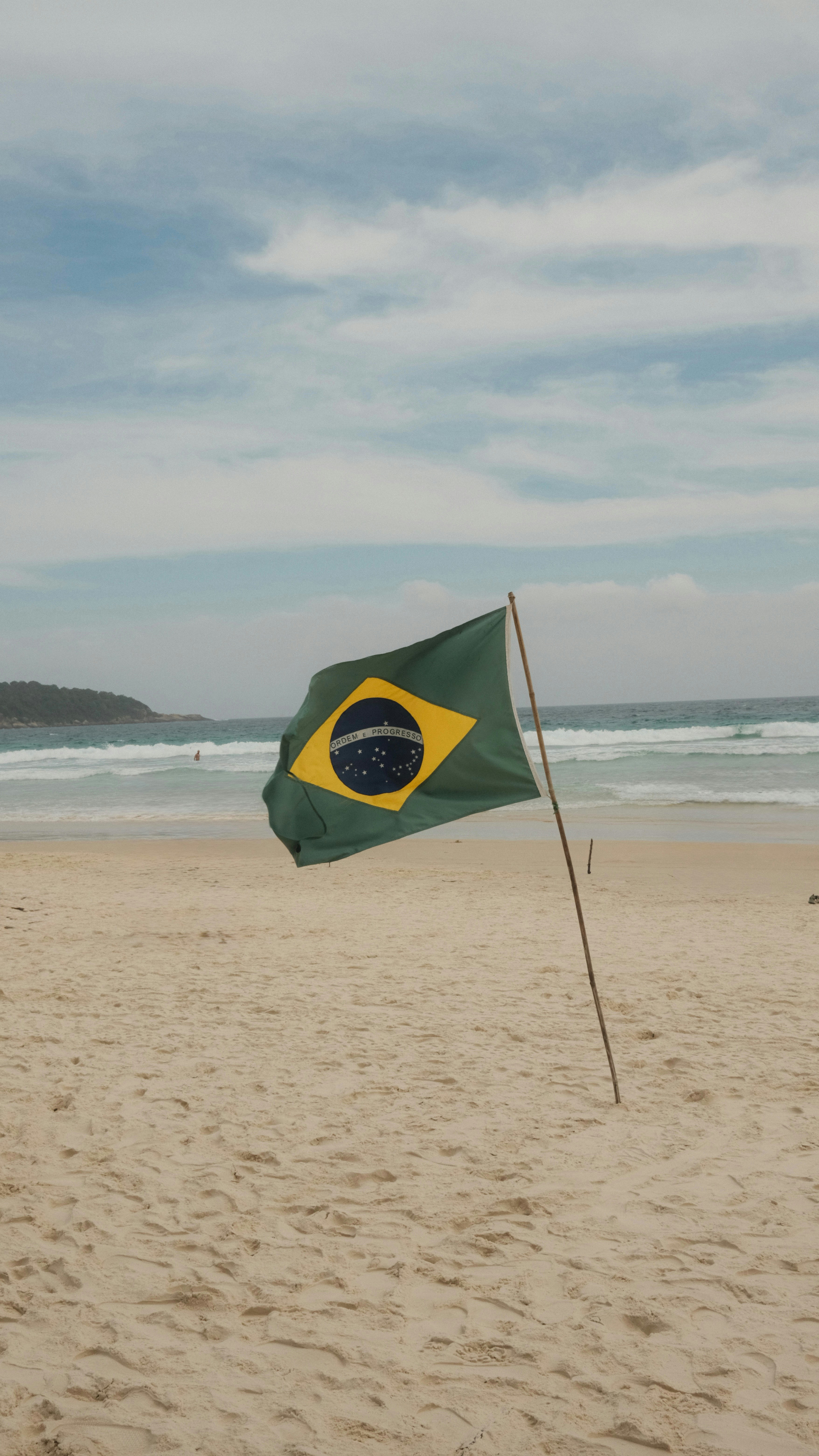 Brazilian flag waving on a sandy beach with ocean waves.