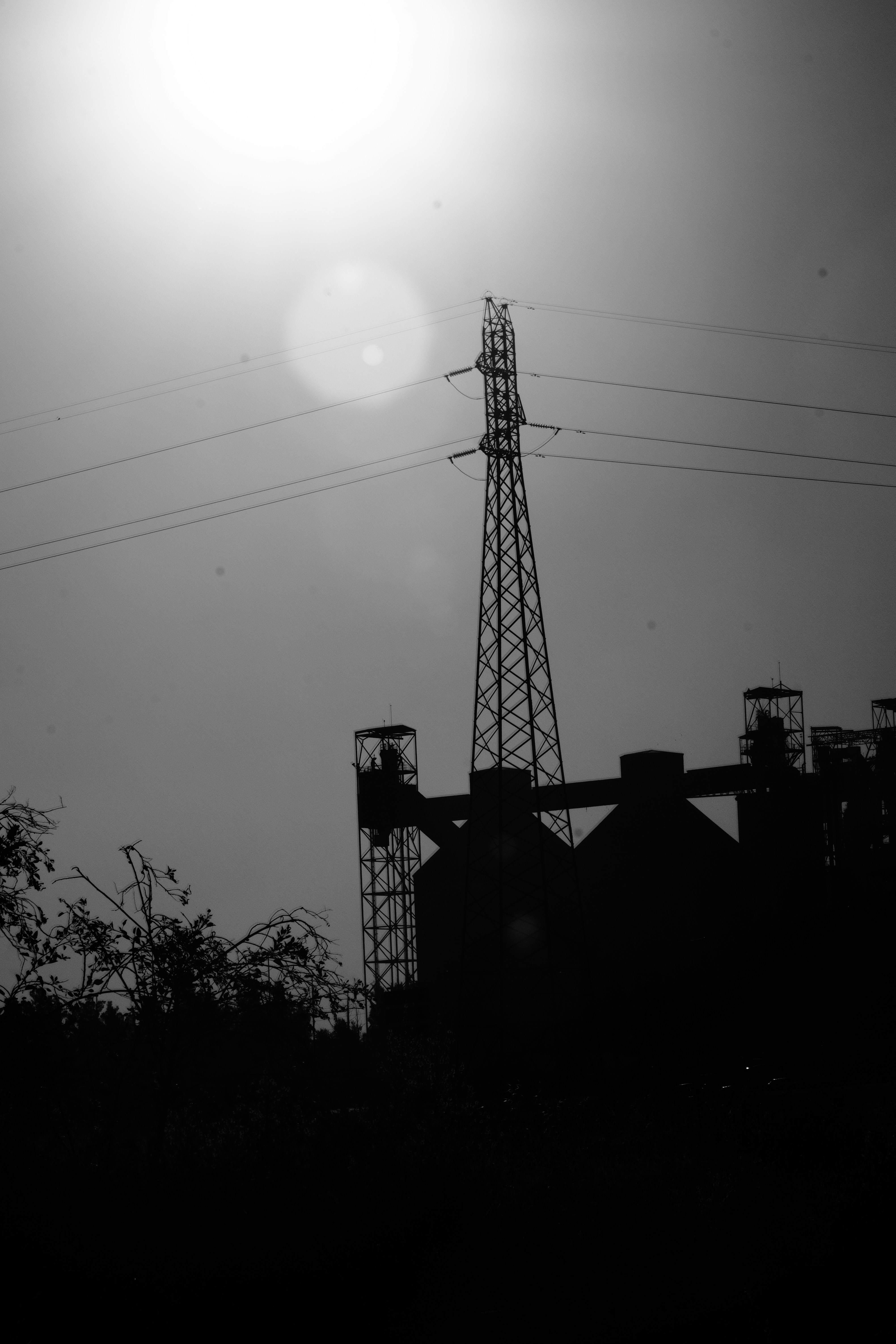 Stark silhouette of a power pylon and industrial buildings.