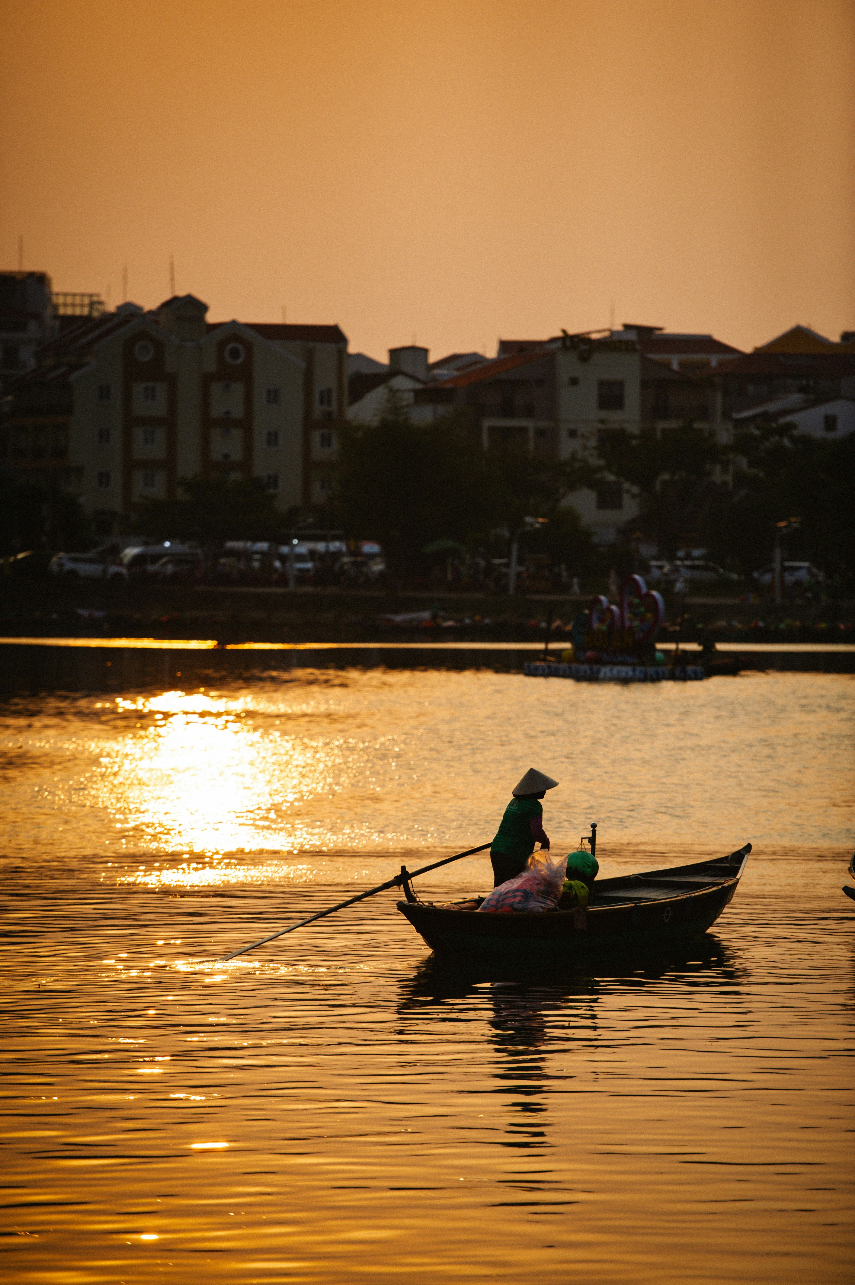 A person rows a boat on golden water at sunset.