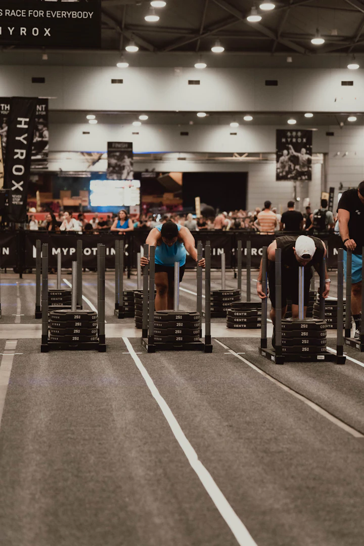 Estação de sled push numa arena de Hyrox com atletas e público