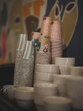 Stacks of colorful paper cups and white ceramic bowls.
