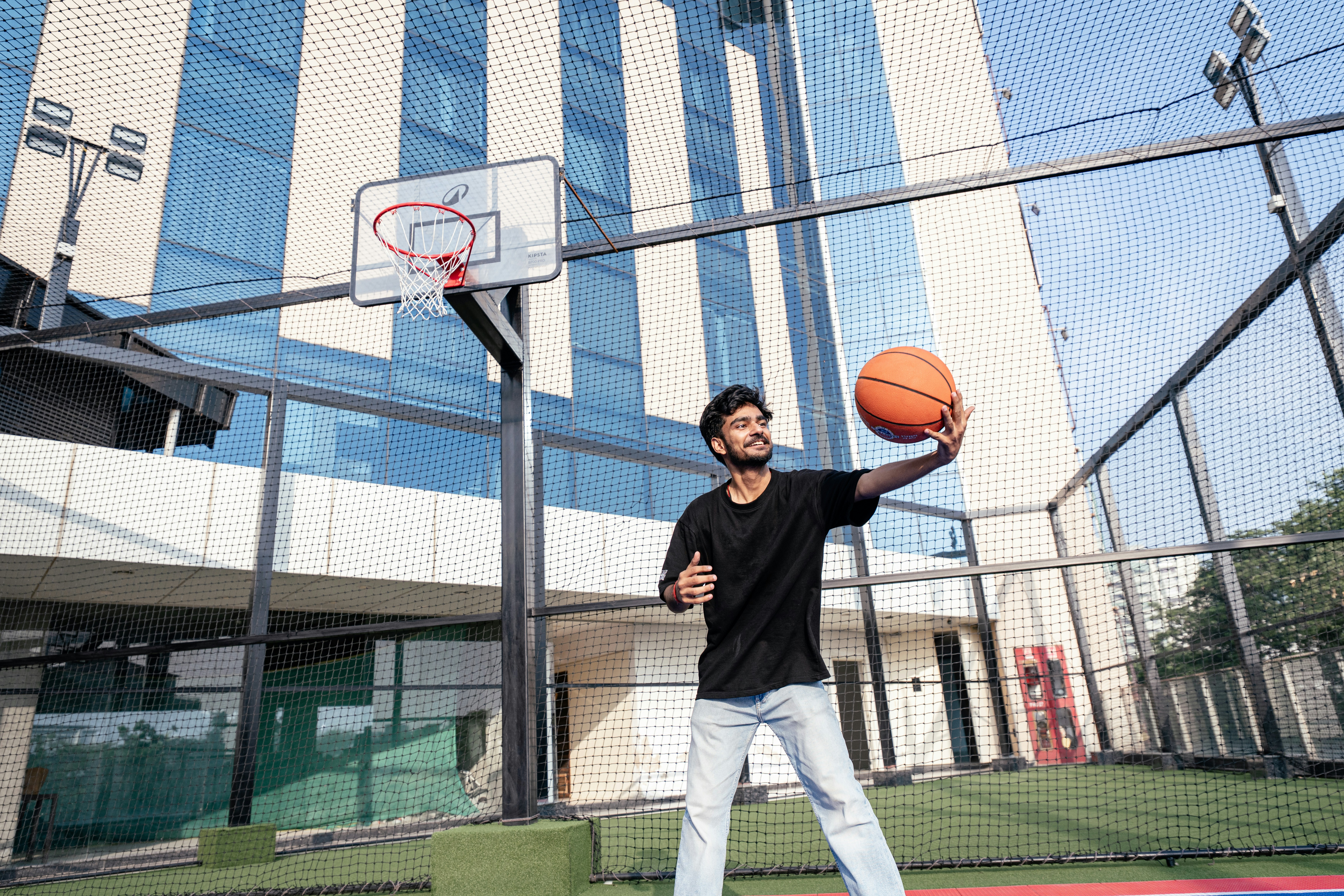 Seorang pria memegang bola basket di lapangan luar ruangan.