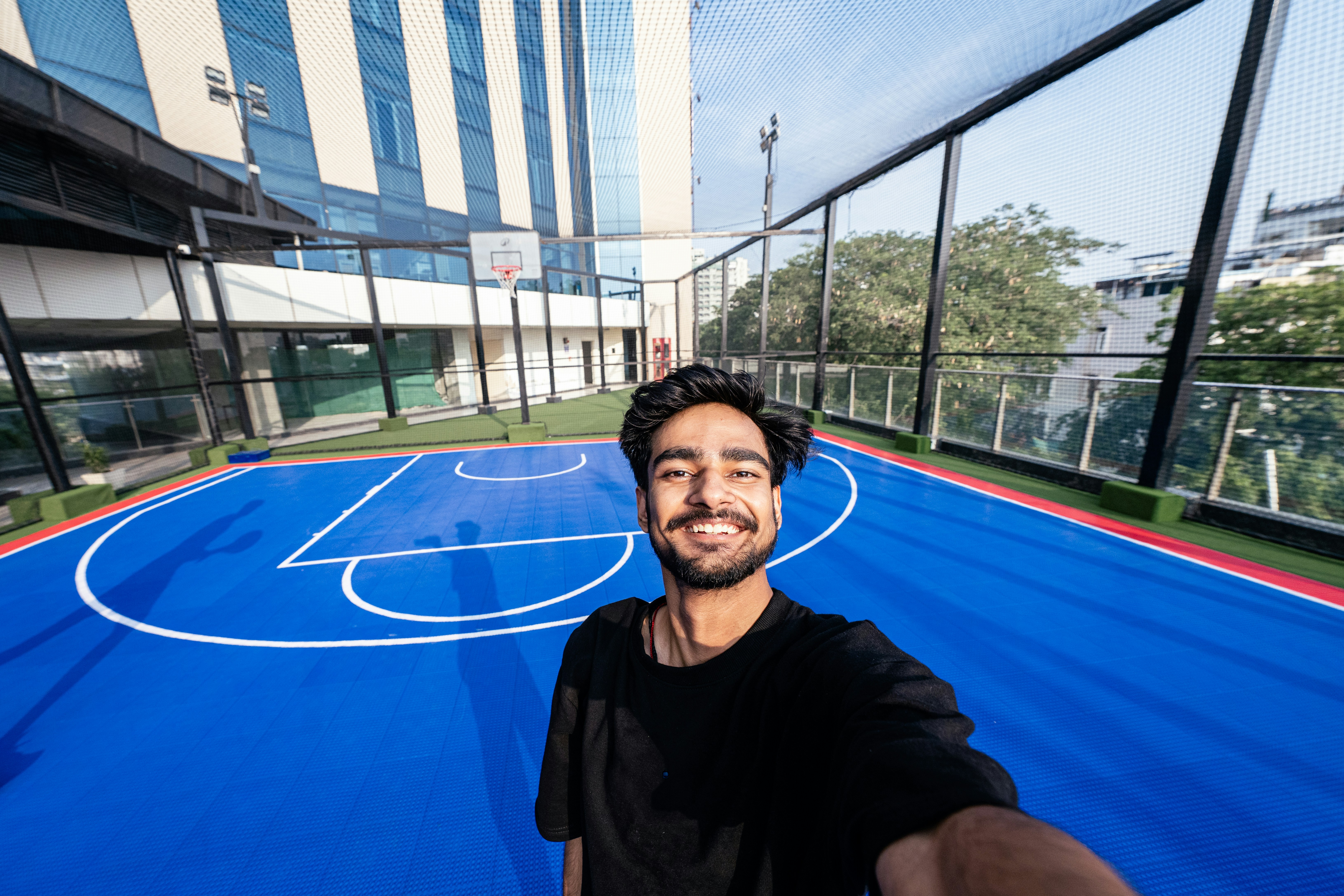 Seorang pria tersenyum di lapangan basket luar ruangan berwarna biru cerah.