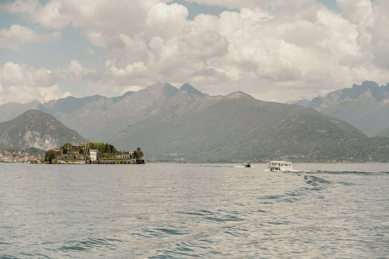 Isola Bella's palace and terraced gardens on Lake Maggiore, with a boat crossing and mountains beyond