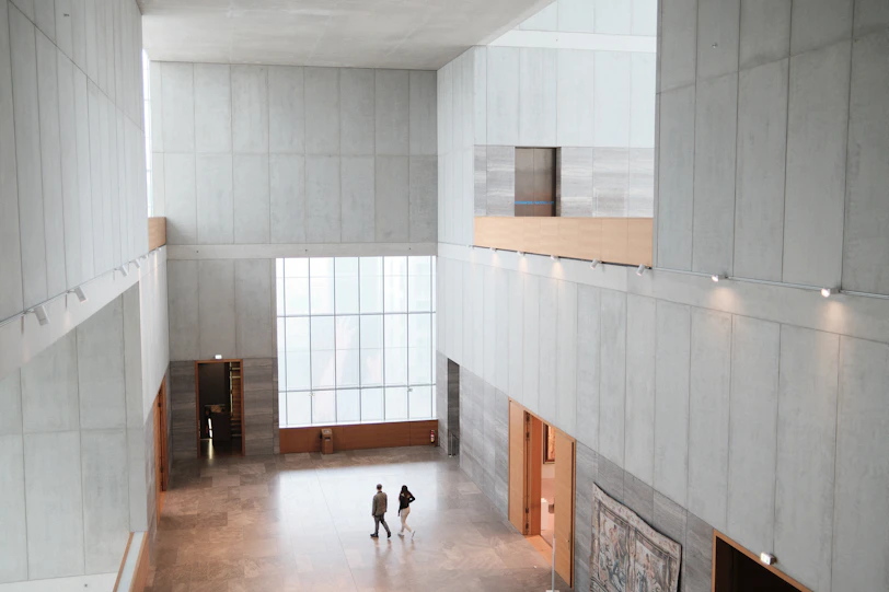 Two people walk in a vast, modern concrete building interior.