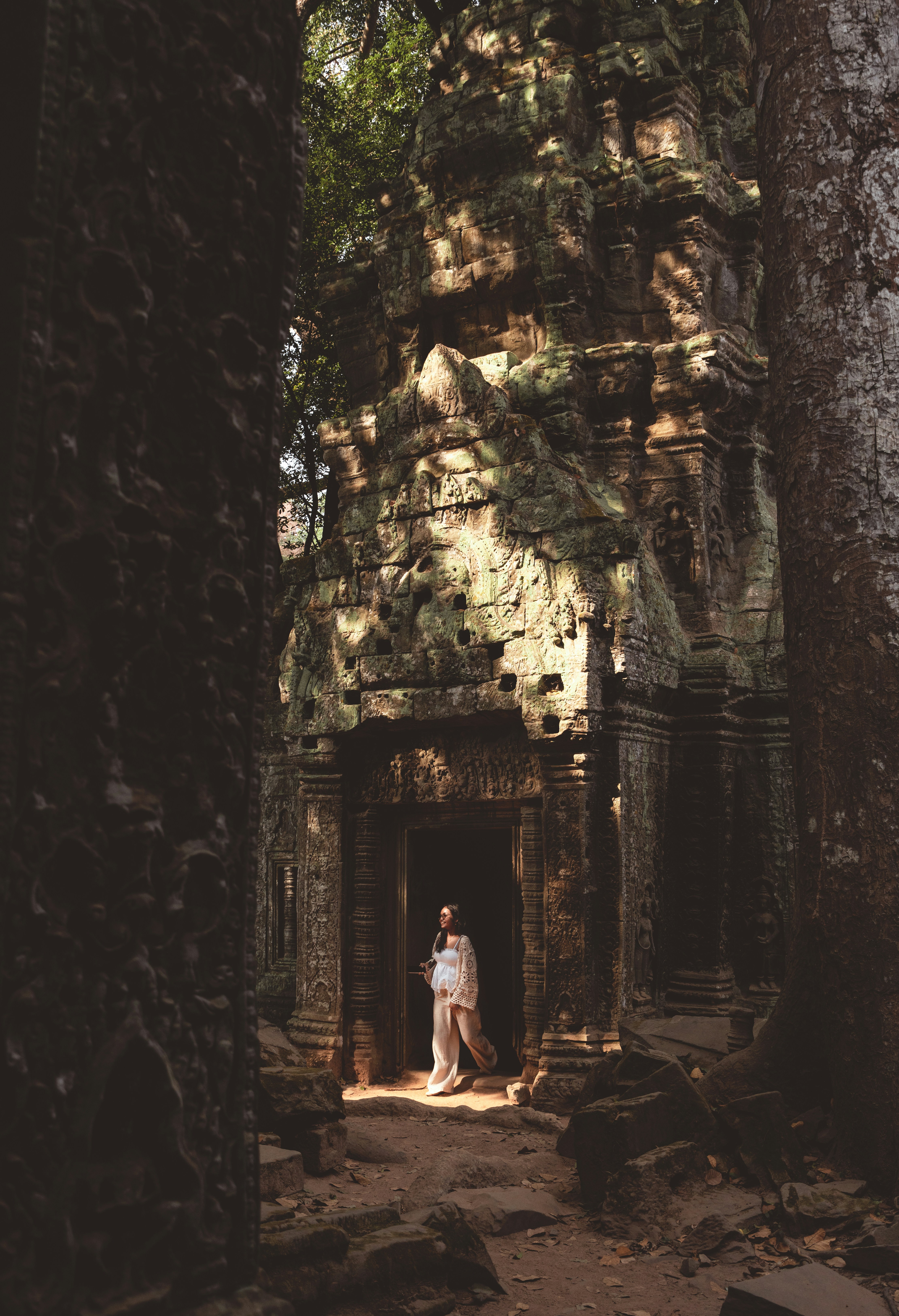 Woman walking from ancient temple entrance framed by trees.