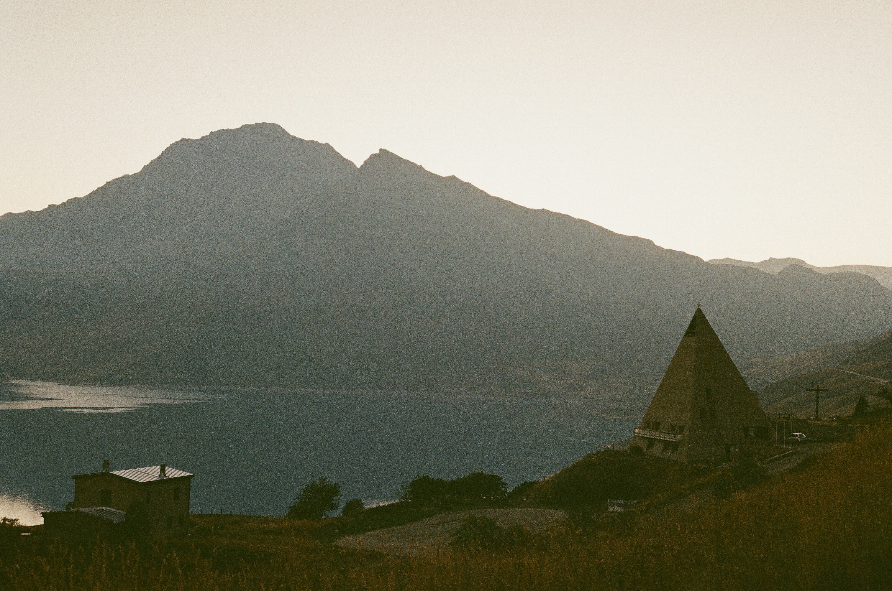 Mountain silhouette, lake, and unique pyramid building at dawn.