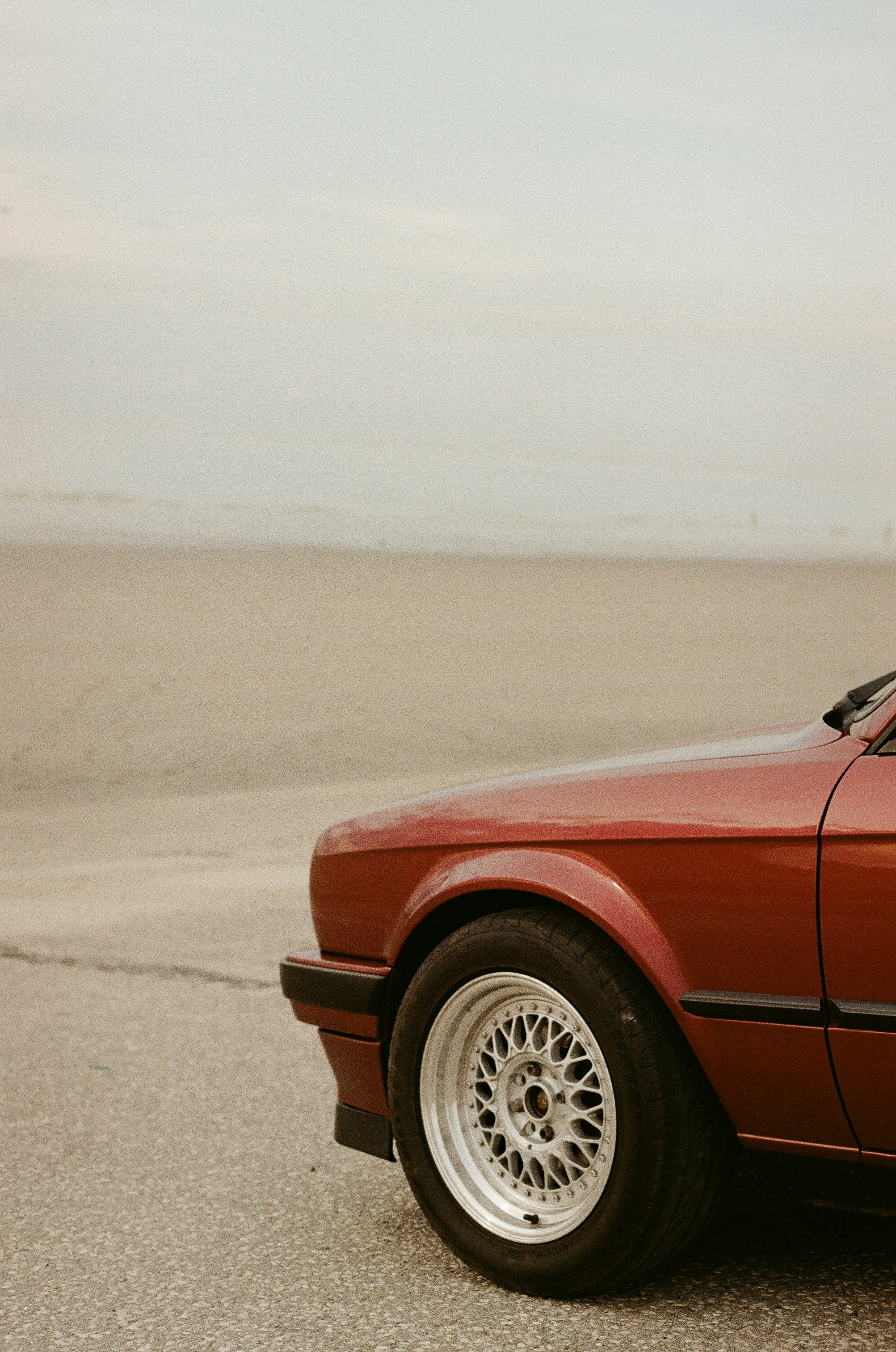 Reddish-brown car on asphalt road with sandy beach background.