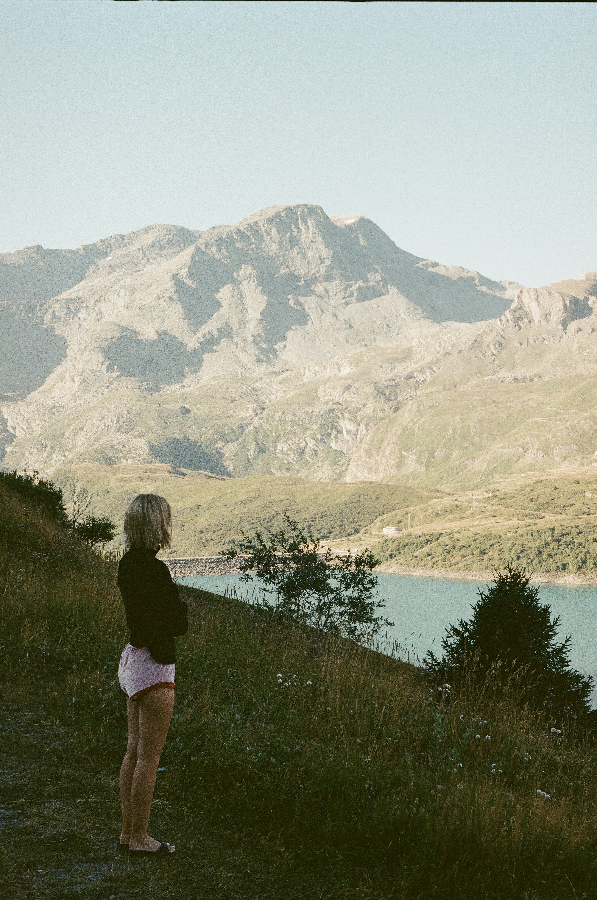 A blonde woman admires a mountain lake landscape.