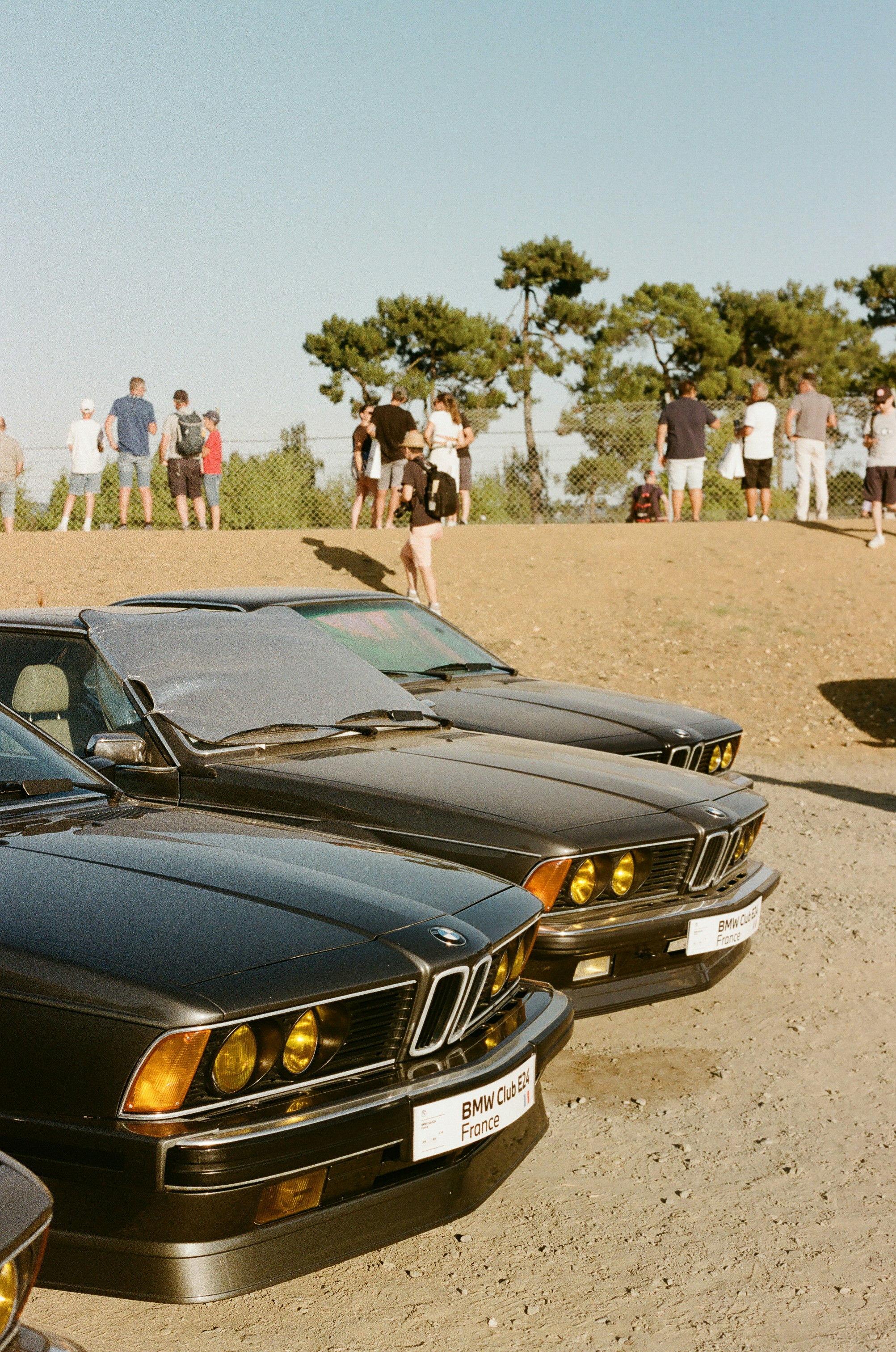 Several vintage black BMW cars parked with people in background.