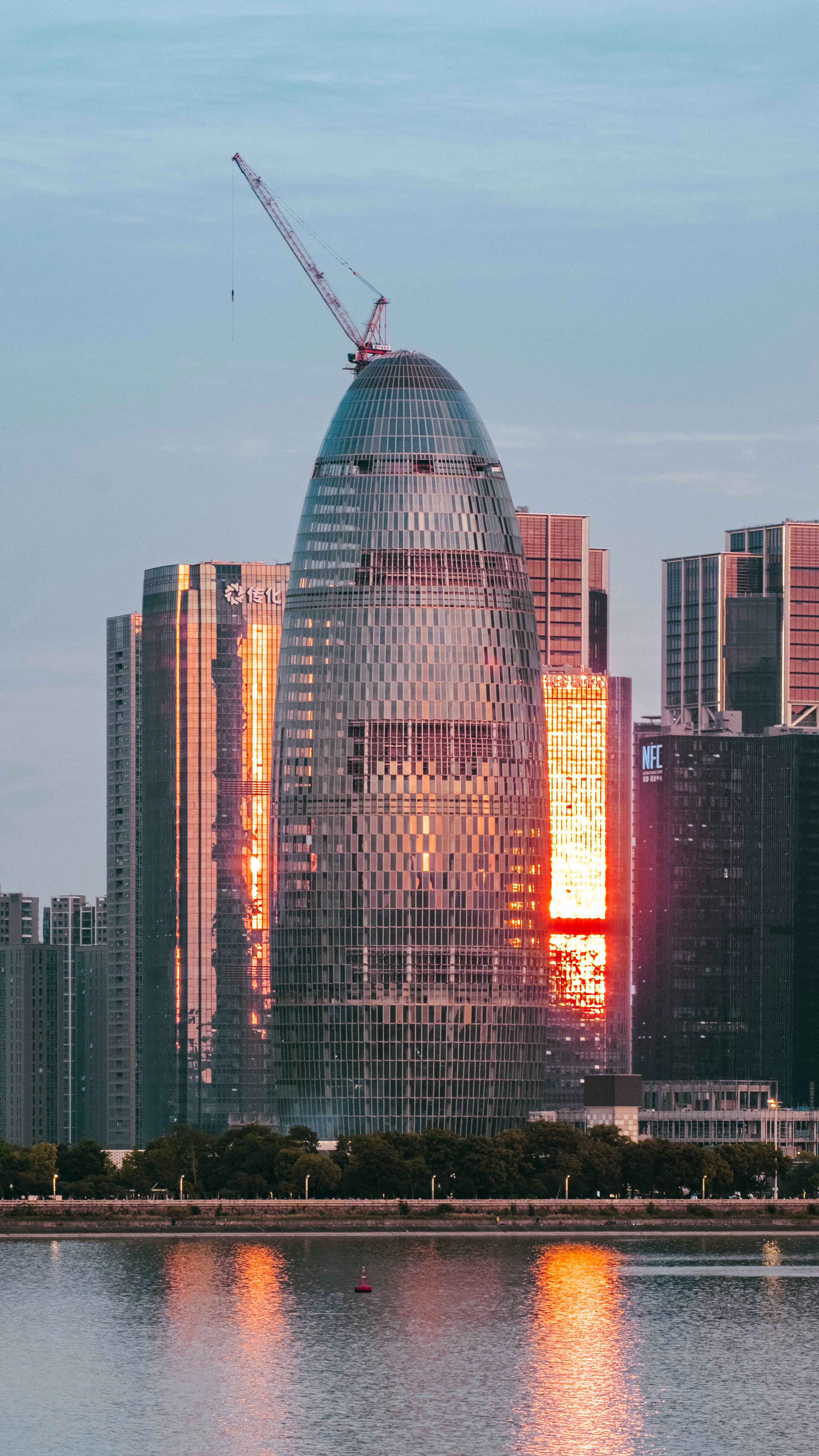 Paisaje urbano moderno con un rascacielos en forma de huevo que refleja el atardecer sobre el agua.