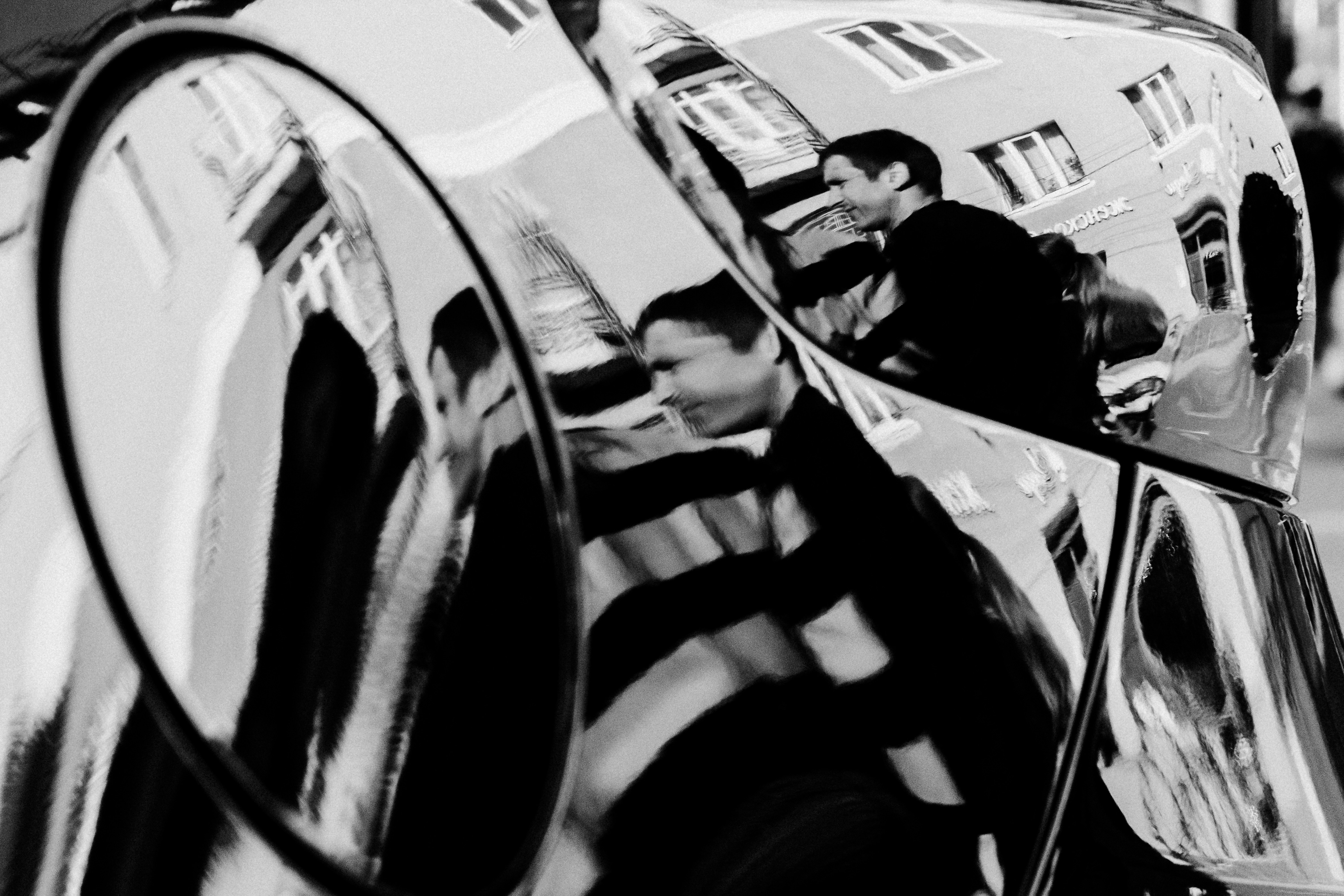 Curved chrome surface reflecting people and architectural details.