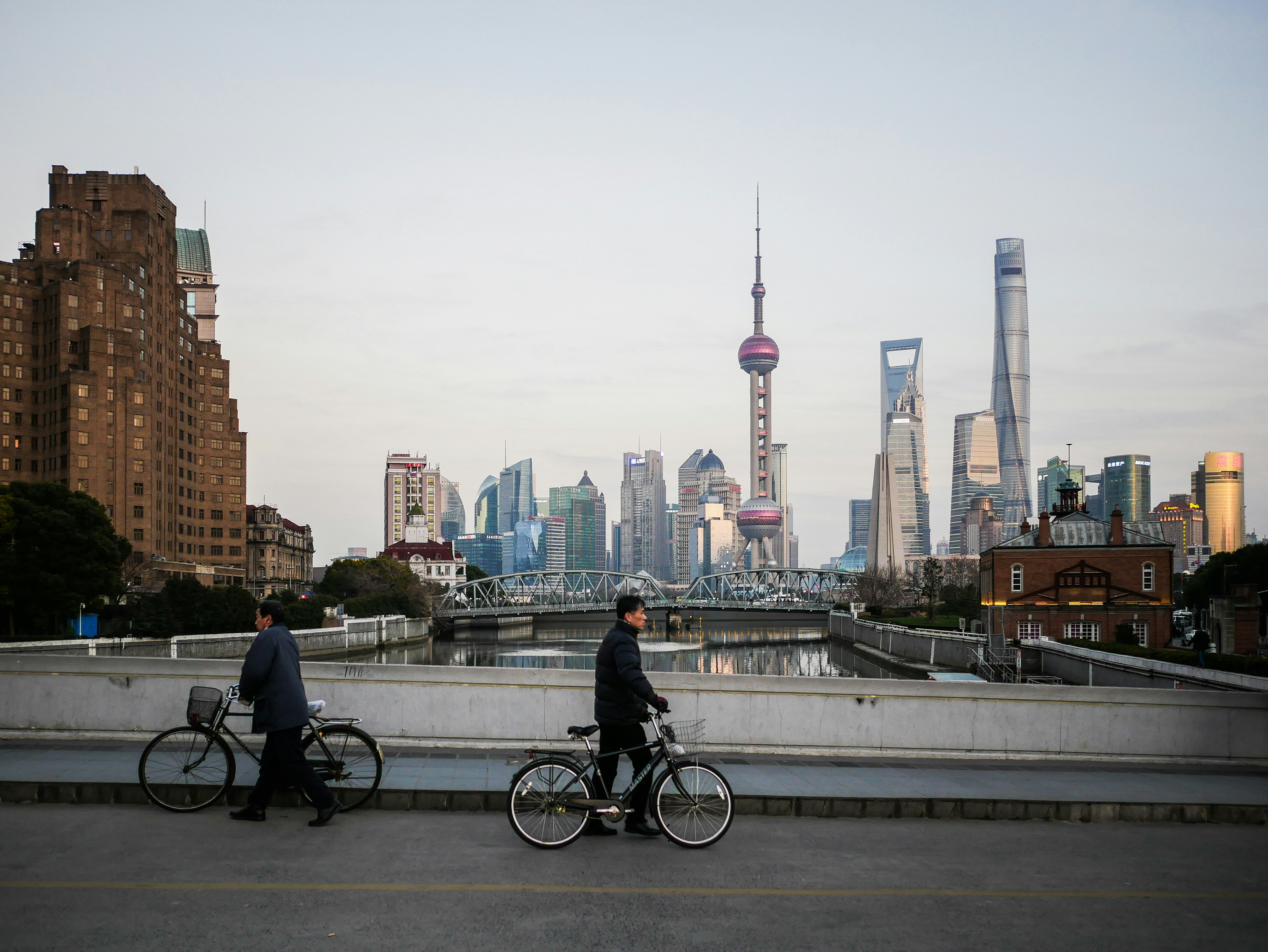 People with bicycles on a bridge with a shanghai skyline.