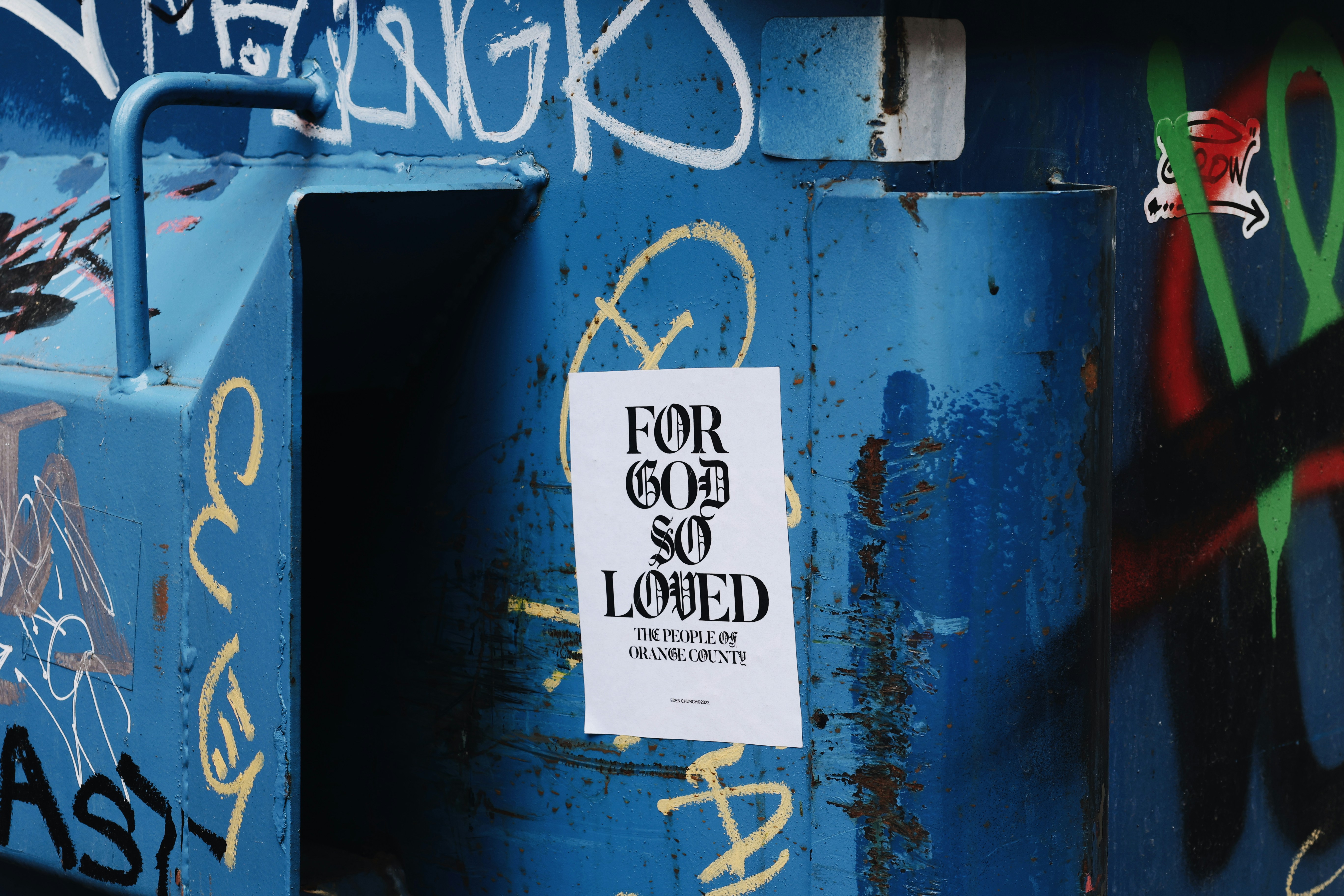 Póster 'para dios tan amado' en una pared azul cubierta de grafitis.