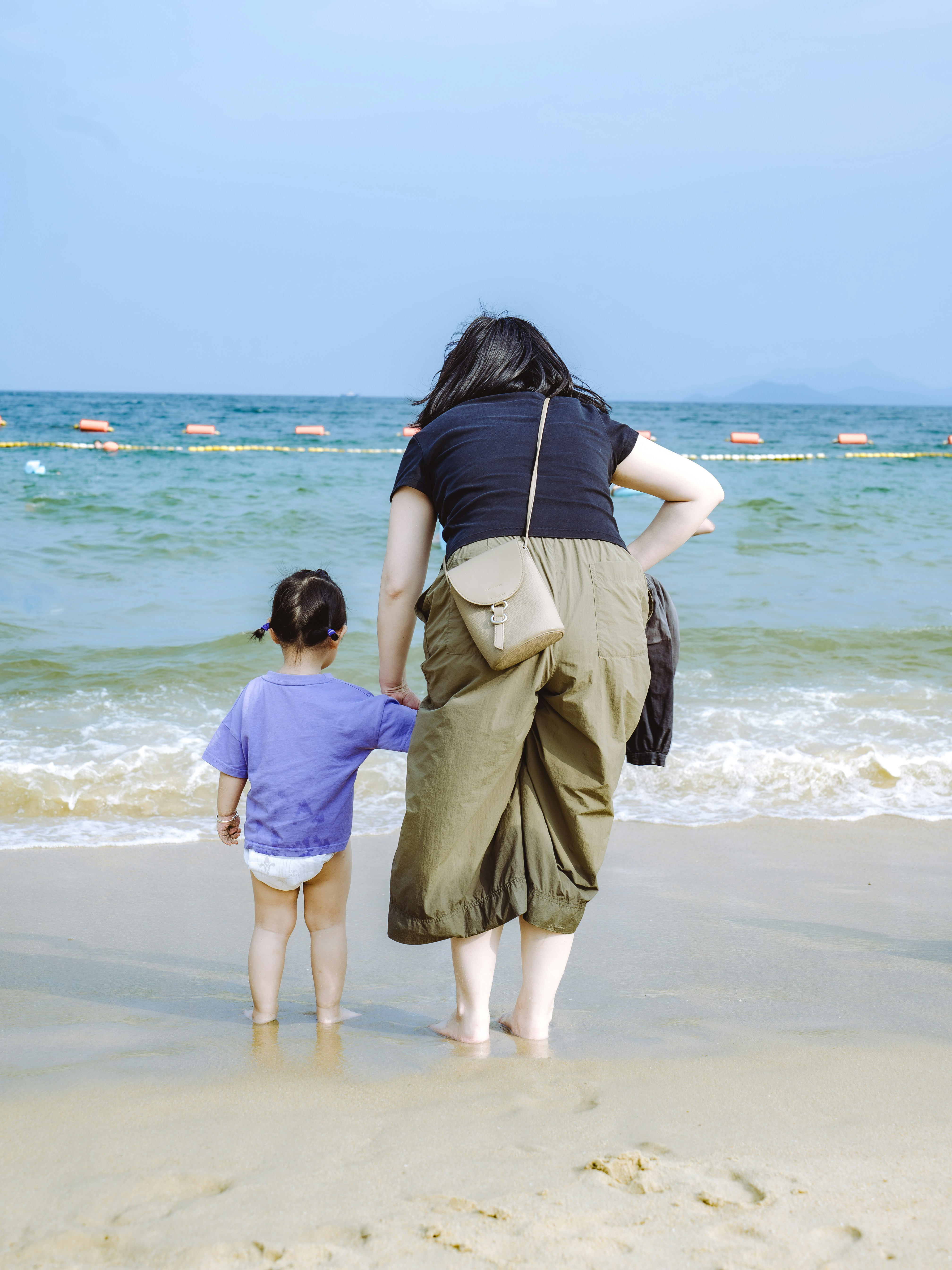 Wanita dan anak berpegangan tangan di tepi laut.