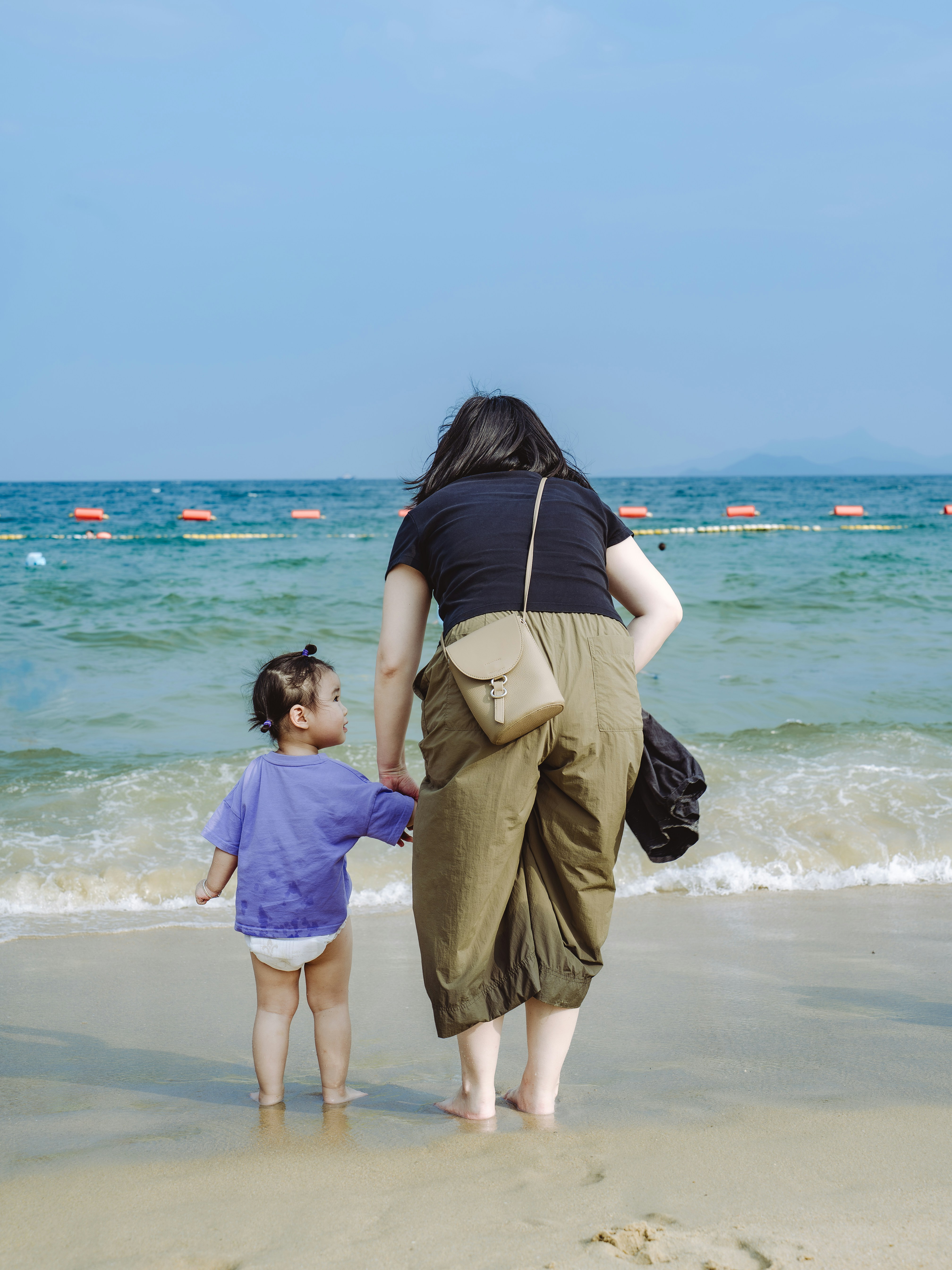 Ibu dan anak di pantai memandangi laut.