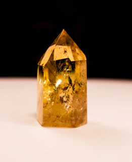 A faceted yellow crystal stands on a white surface.
