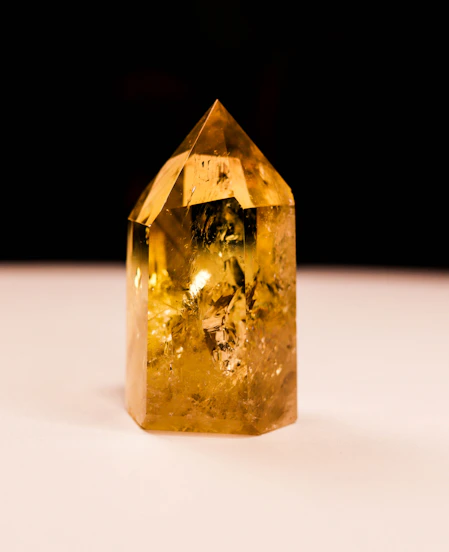 A faceted yellow crystal stands on a white surface.