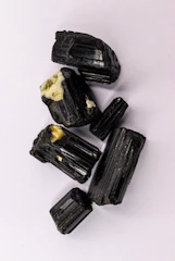 Rough black tourmaline crystals on a white surface.