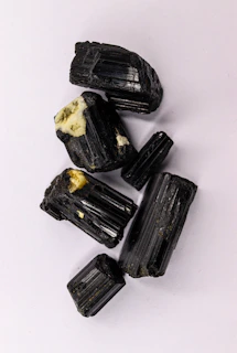 Rough black tourmaline crystals on a white surface.
