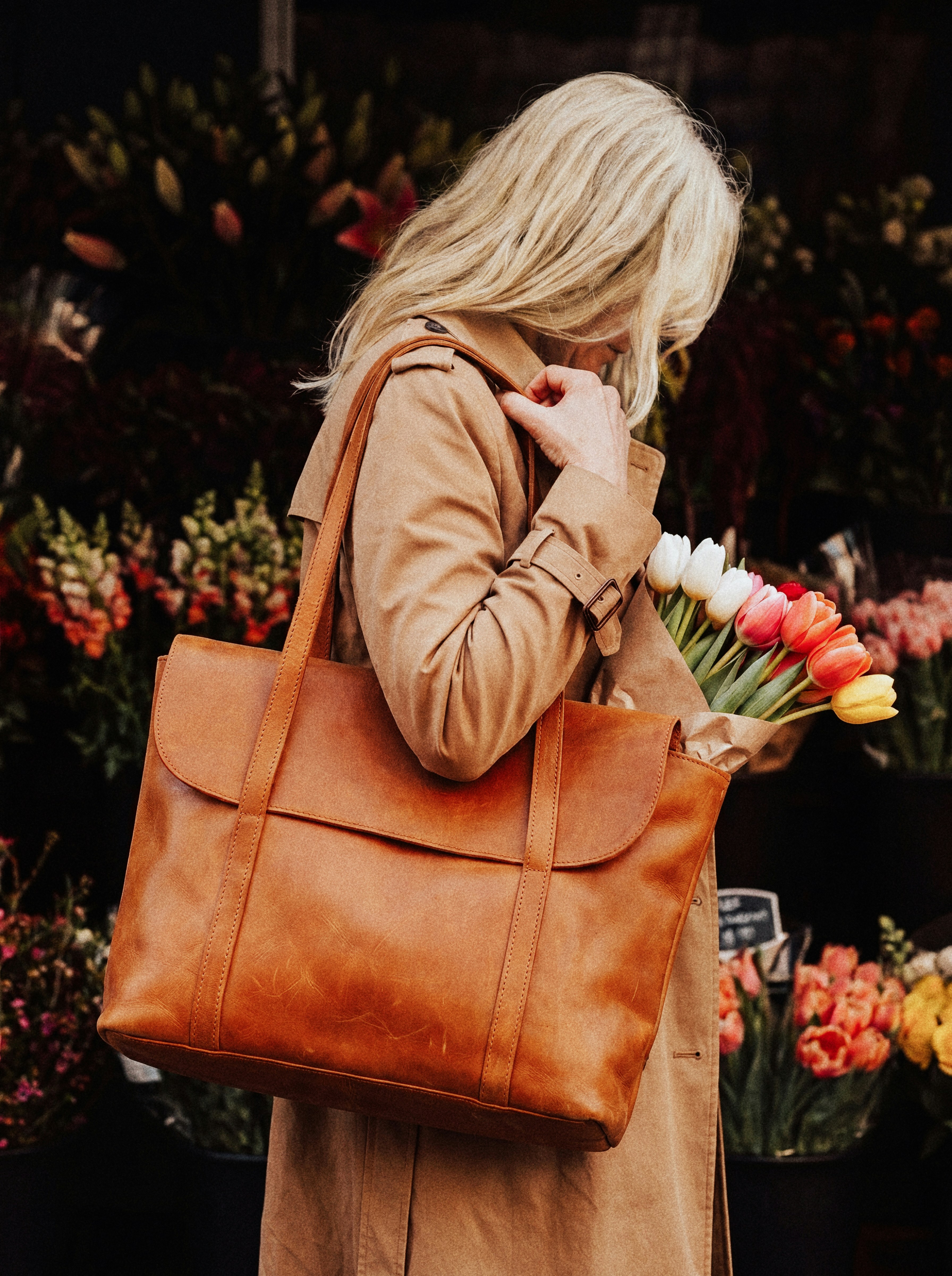 A woman with a brown bag buying flowers.