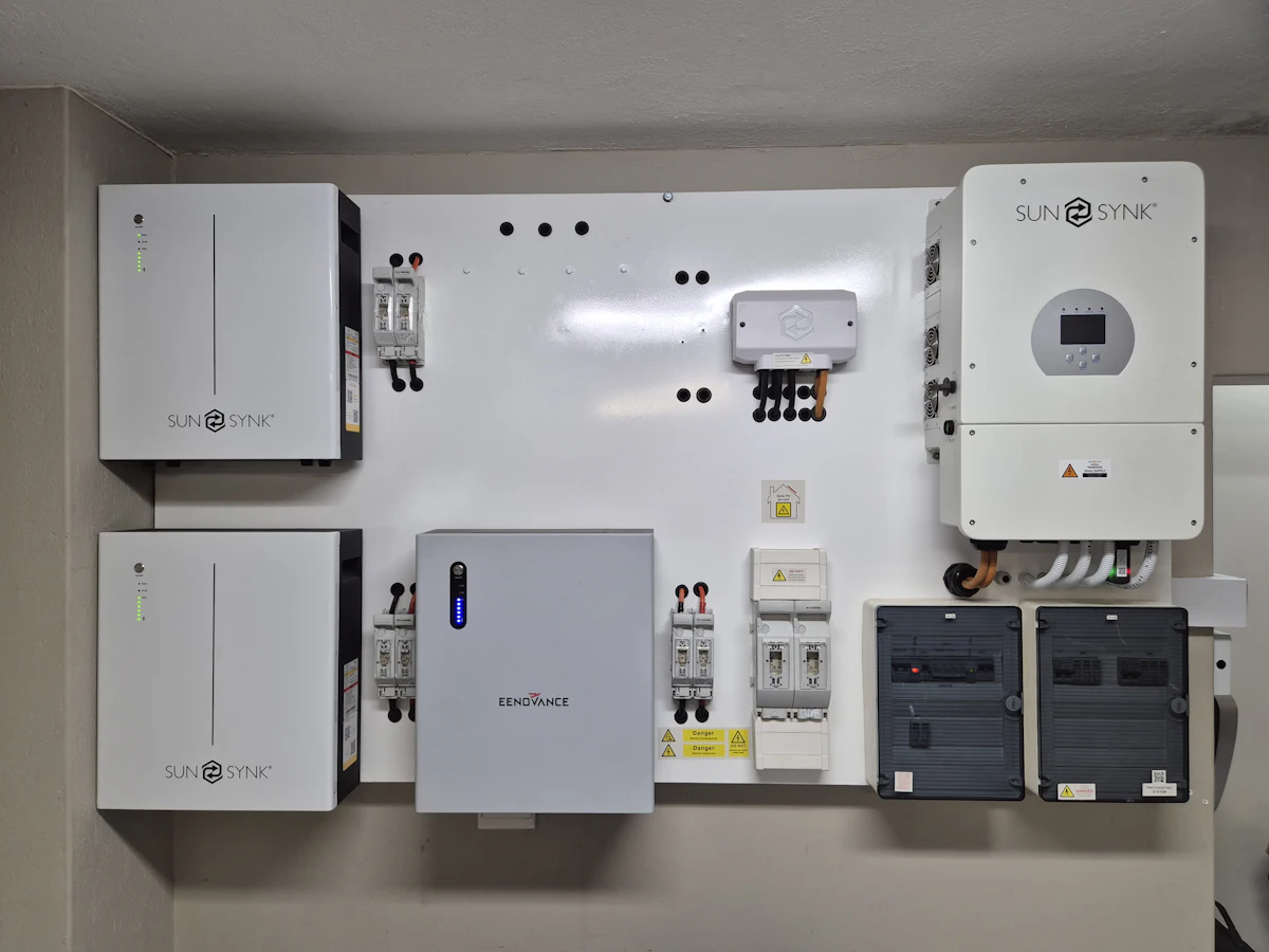 A wall-mounted battery and inverter installation: white cabinets, a combiner box and grey isolators wired together on a plain wall.