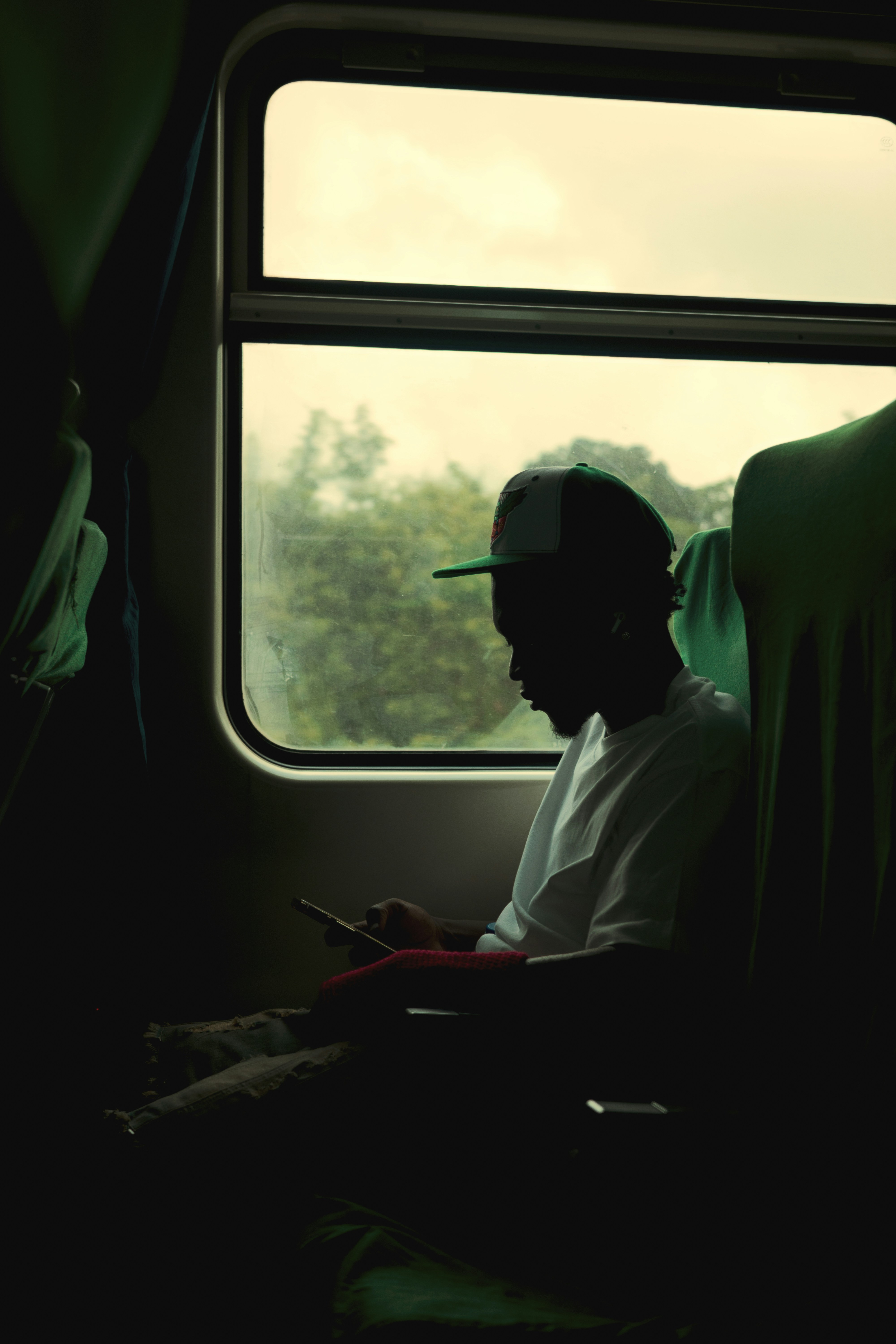 Person in silhouette using a phone by a train window.