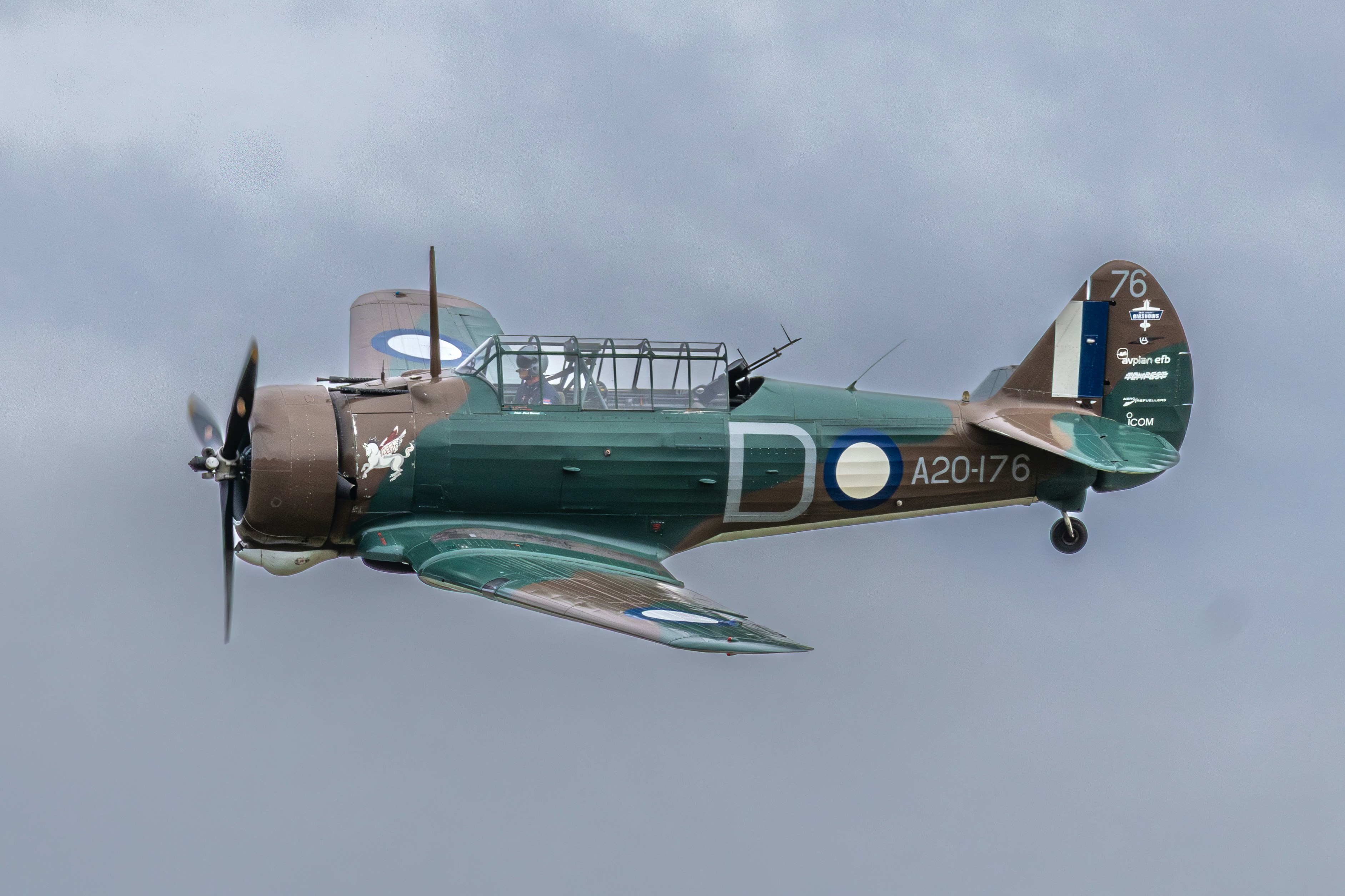 Avion historique à hélice camouflée volant sous un ciel nuageux.