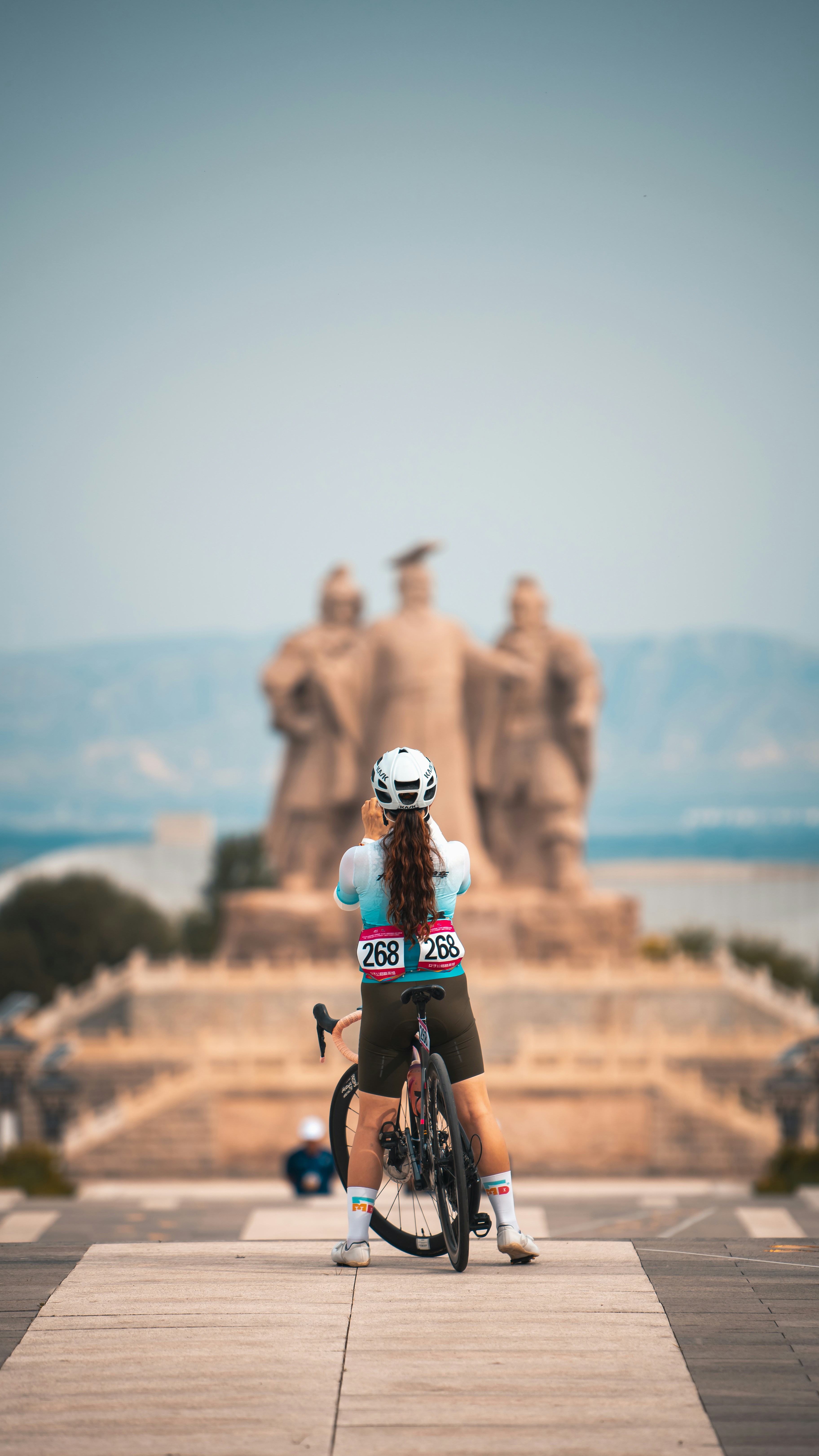 Cyclist with bike looking at a large statue over water.