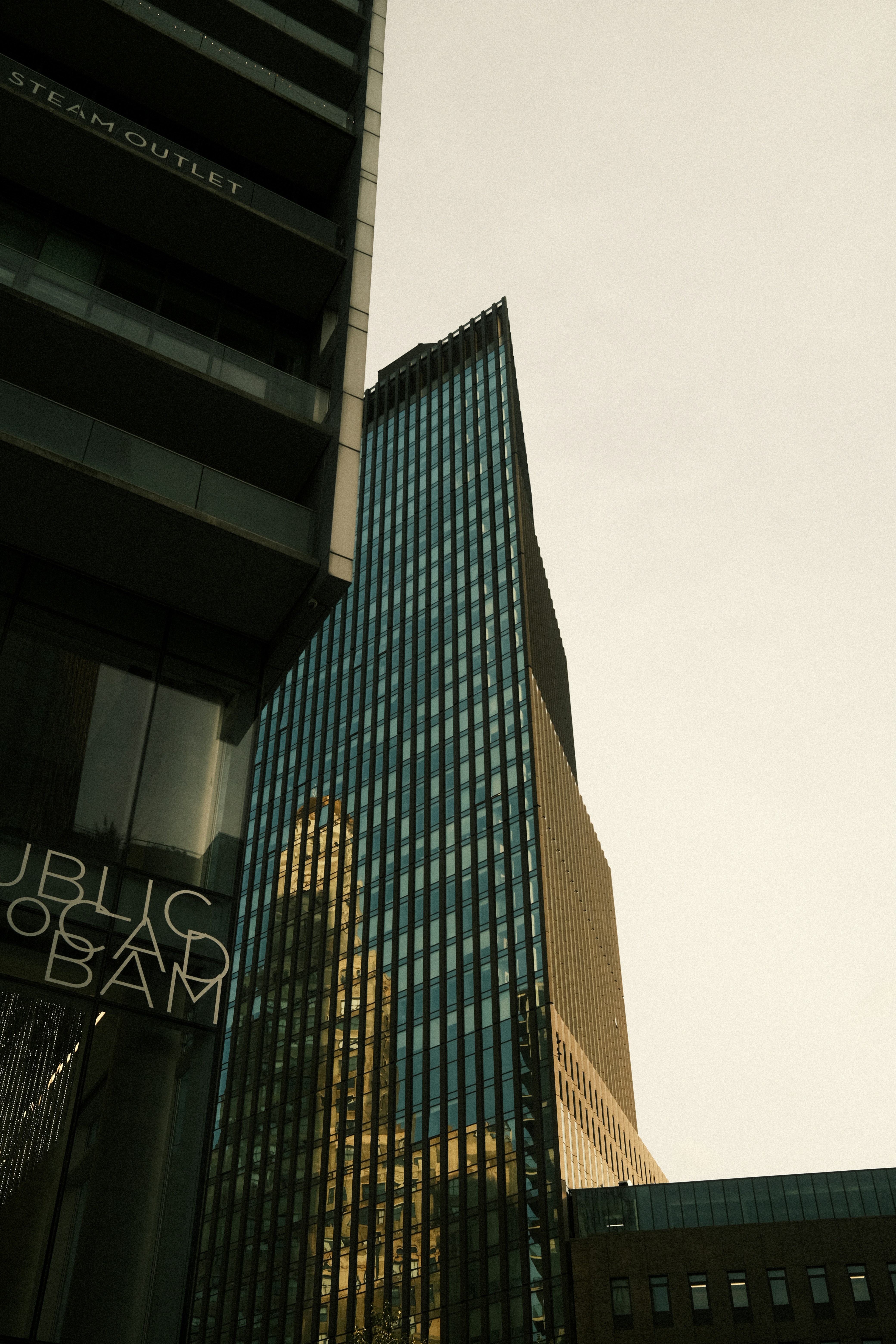 Tall glass skyscraper reflects city buildings against a clear sky.