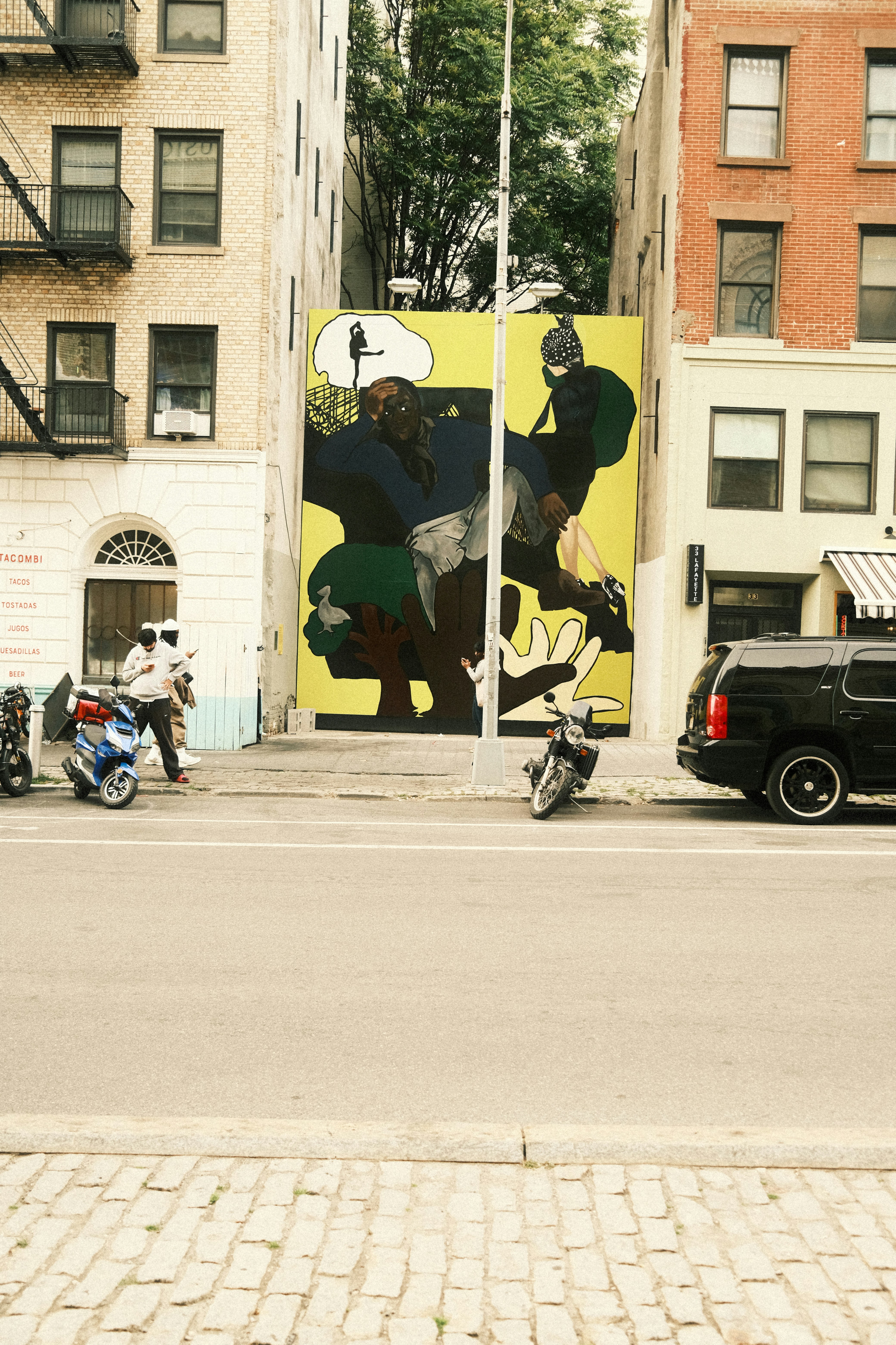 Urban street with colorful mural, buildings, and parked vehicles.