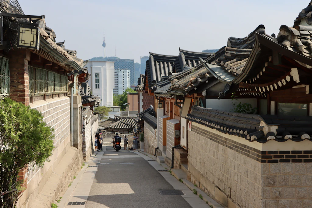 Sloping lane between tiled-roof hanok houses in Bukchon, with modern Seoul beyond