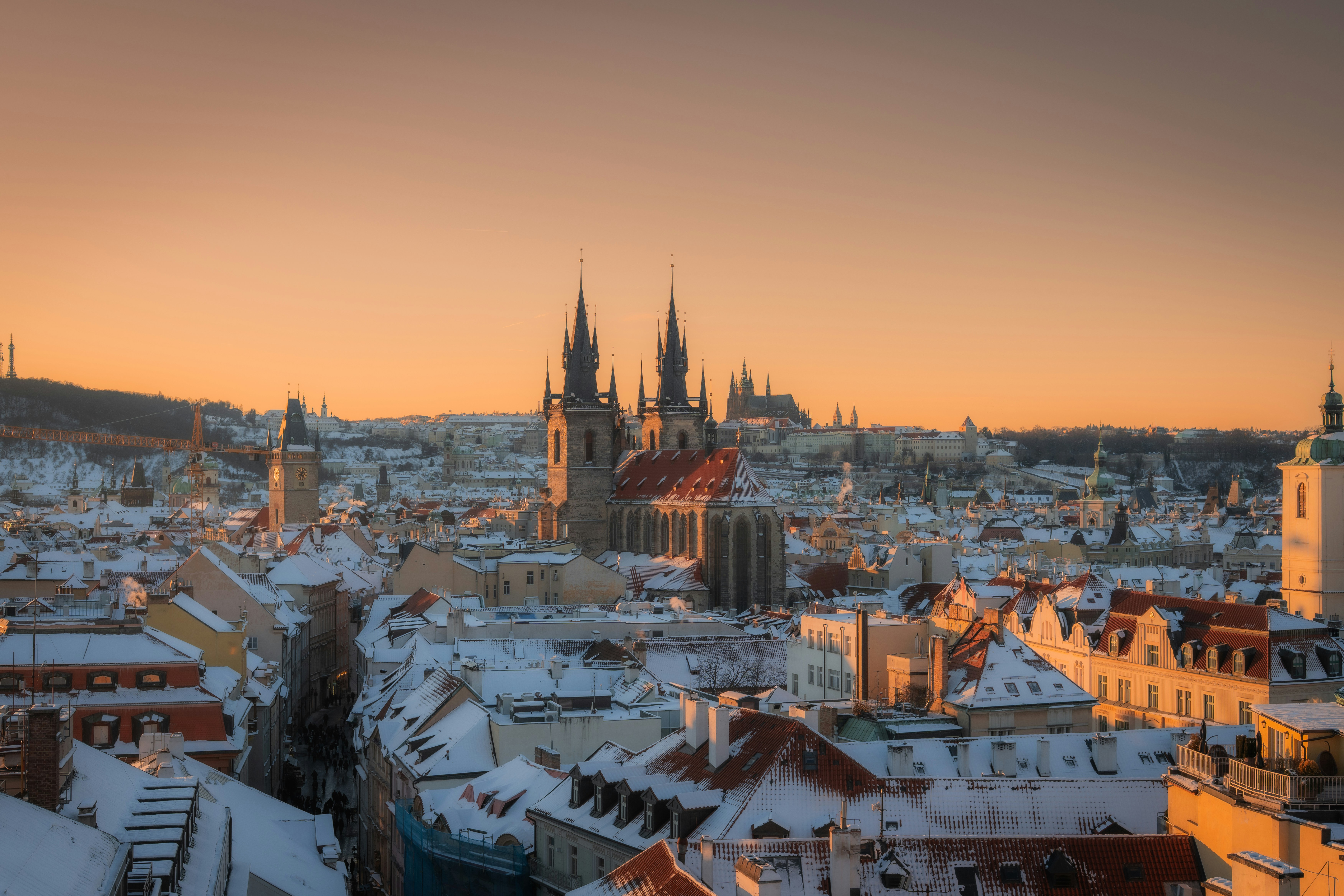 Snowy prague cityscape with historical buildings at sunset.