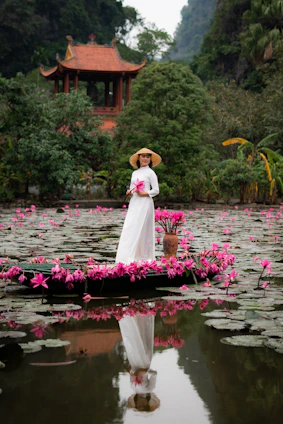 Woman in white dress on boat with pink flowers, pagoda