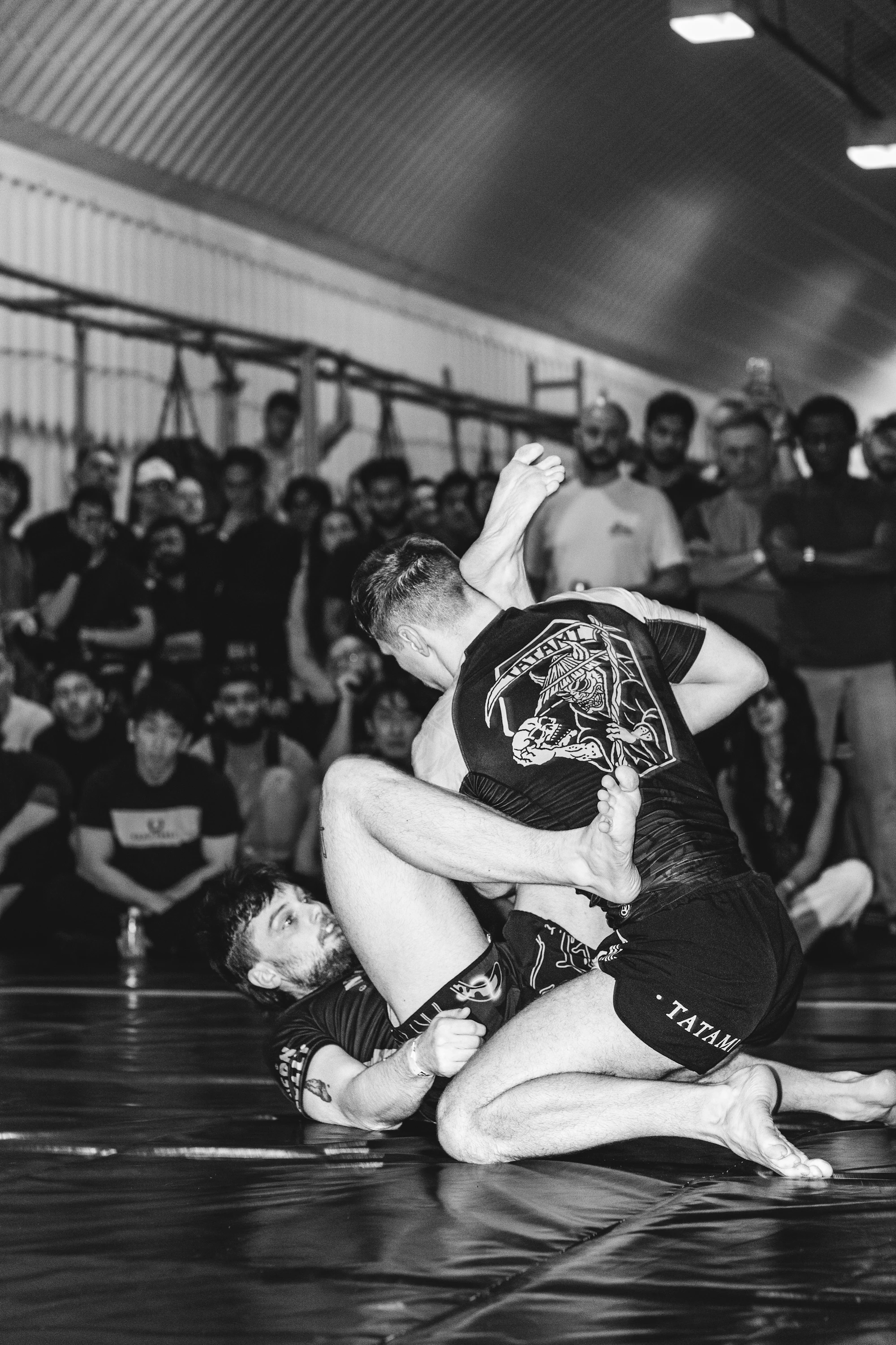 Two athletes grappling on a mat while others watch