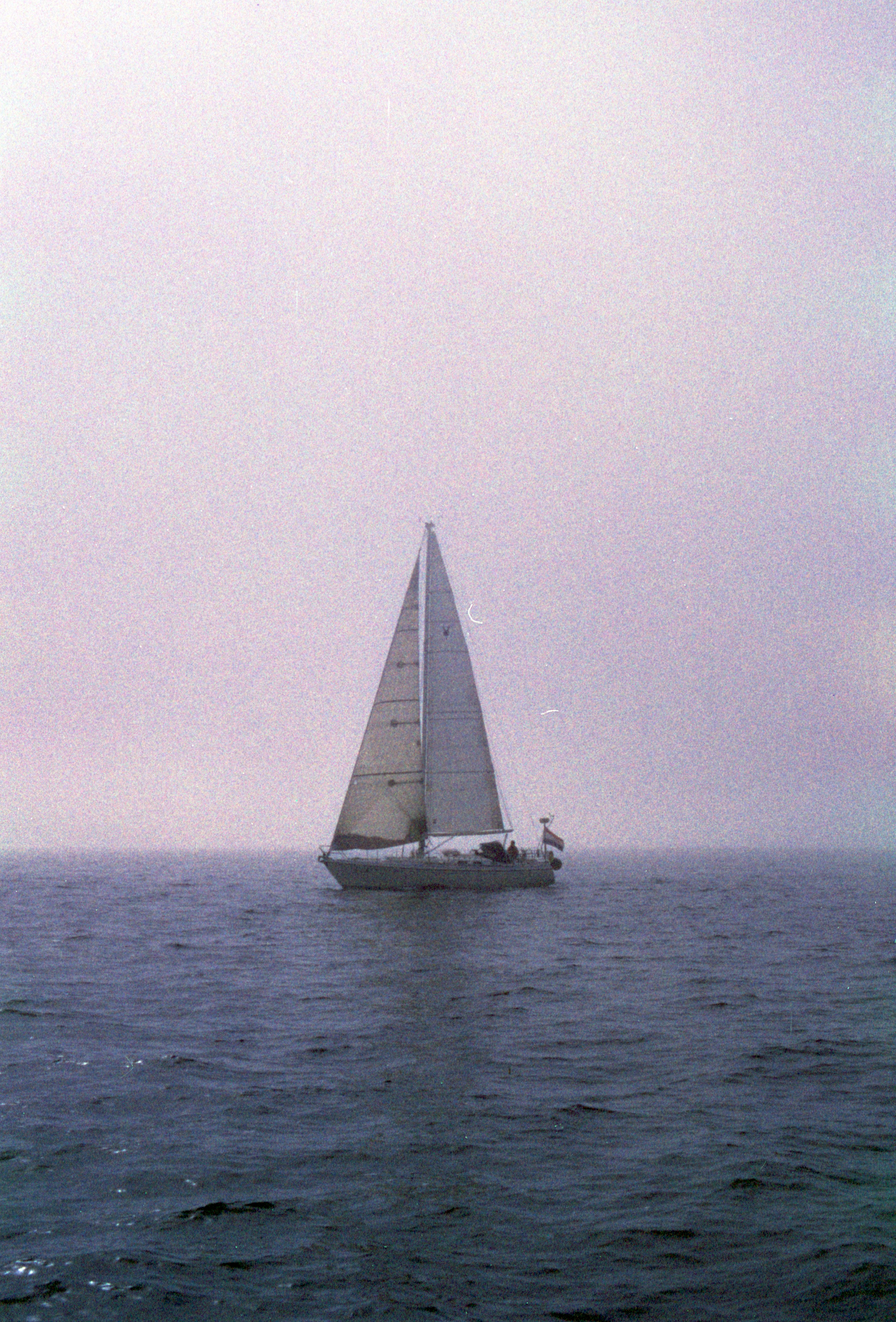 A sailboat floats on a calm, foggy ocean.
