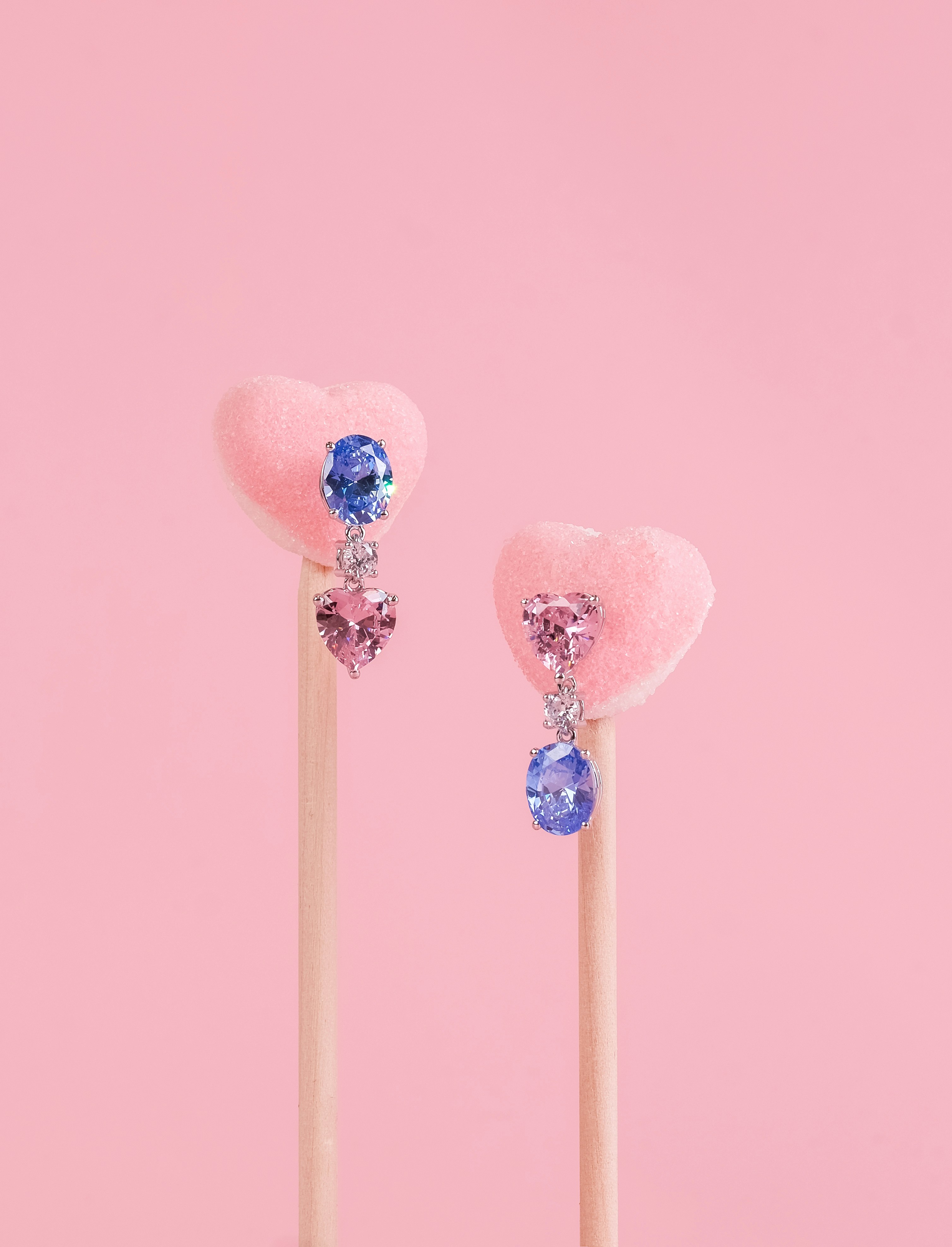 Dangling gemstone earrings displayed on two pink heart lollipops