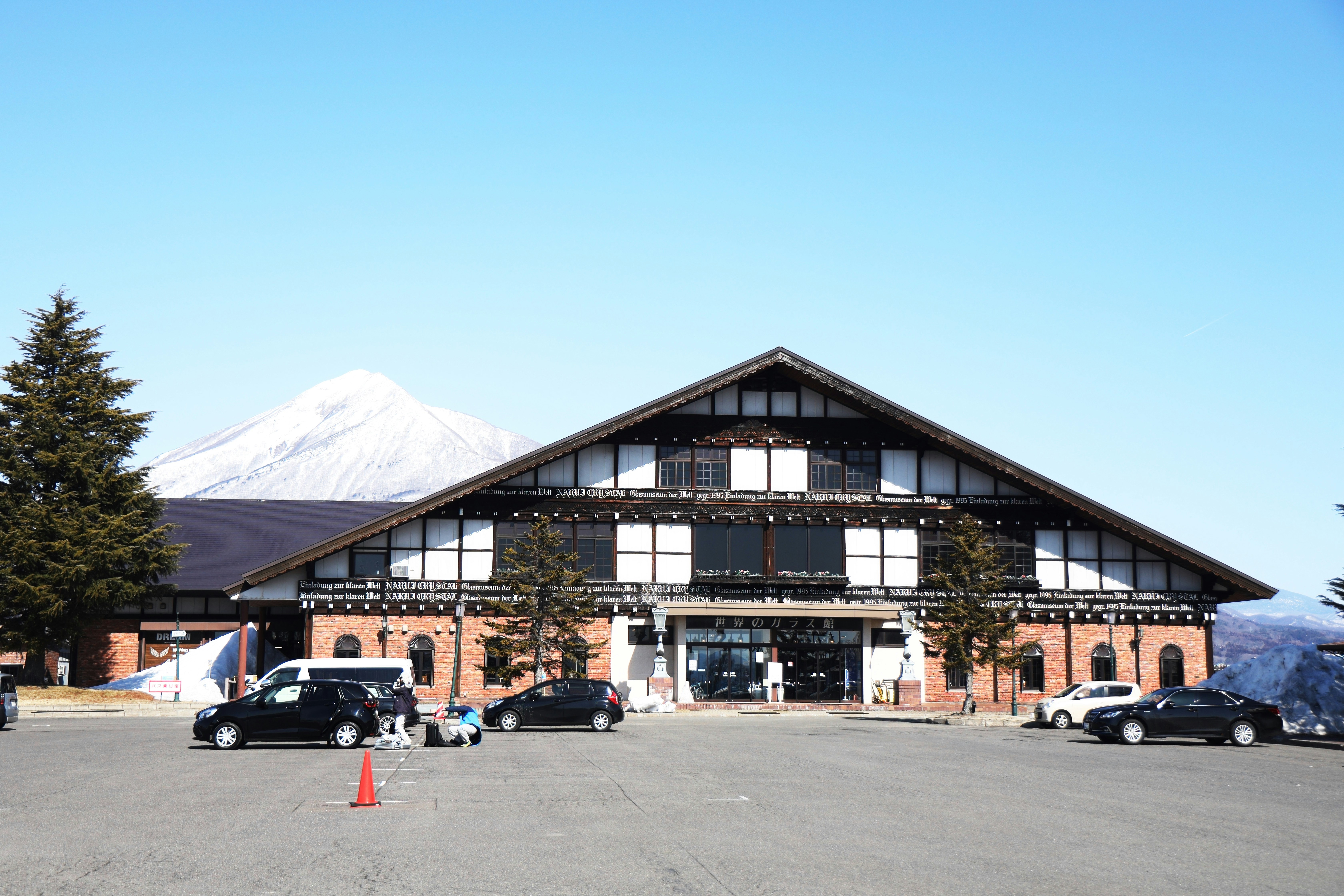 Large building, parking lot, and snow-capped mountain under blue sky.