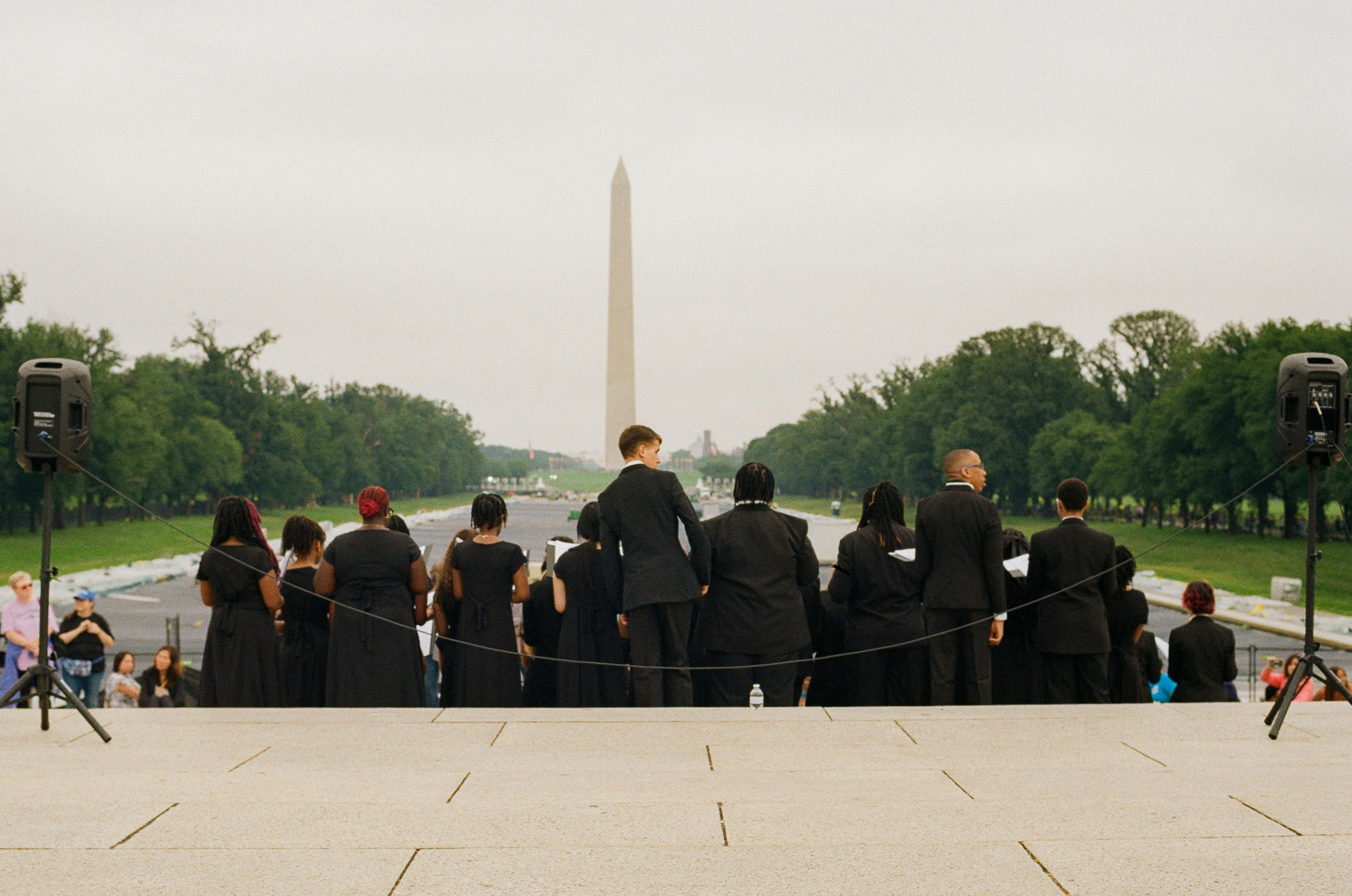 Sekelompok orang berbaju hitam menghadap monumen washington.
