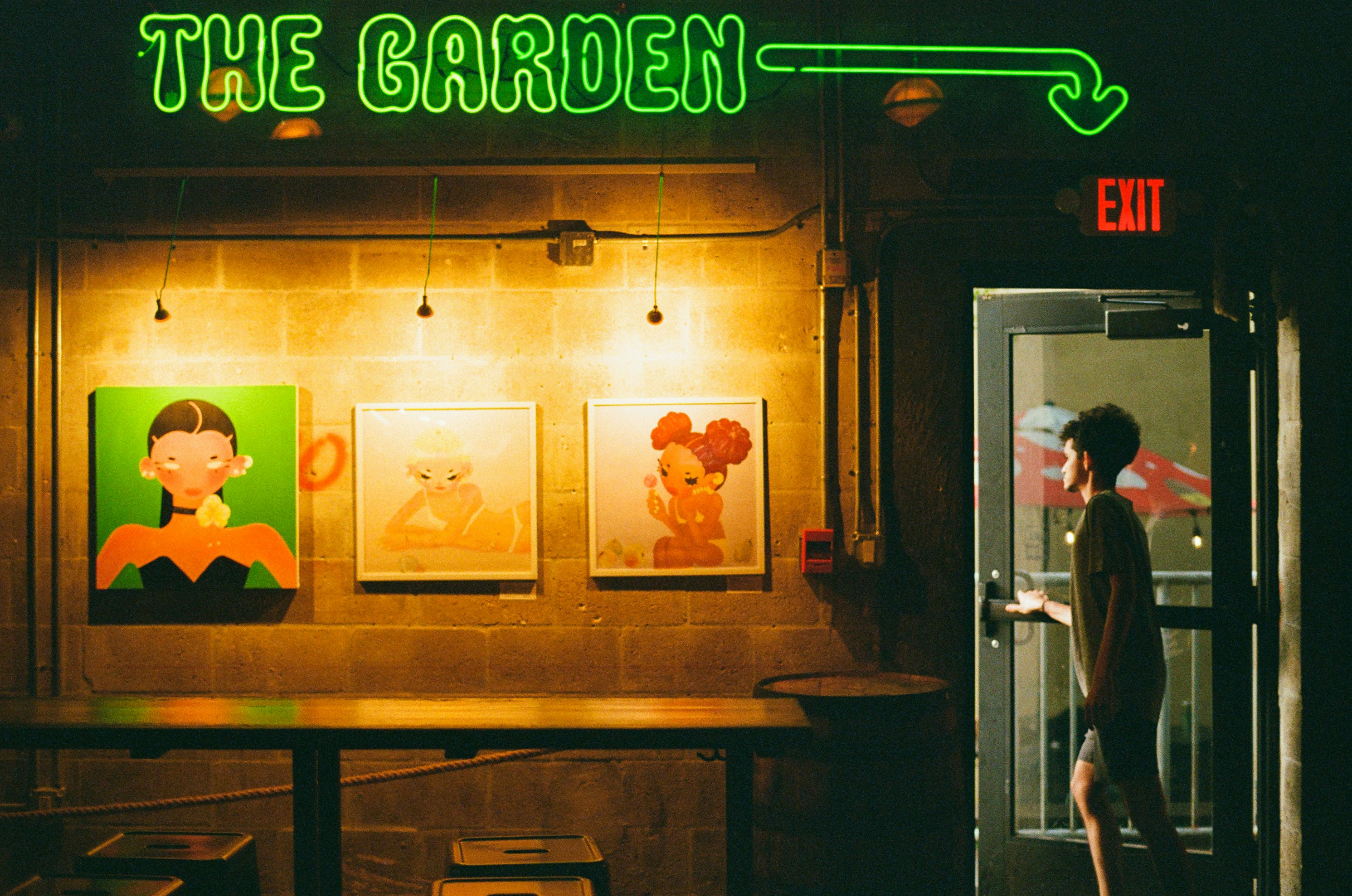 Orang berjalan melalui pintu di bawah tanda neon 'taman'.