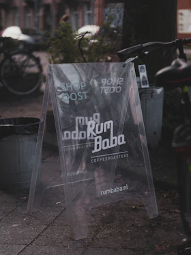 Transparent a-frame sign for rum baba coffee roasters on sidewalk.
