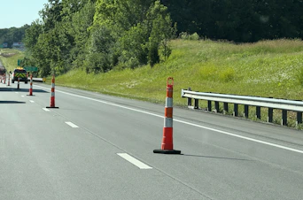 Highway with traffic cones, guardrail, and green landscape.