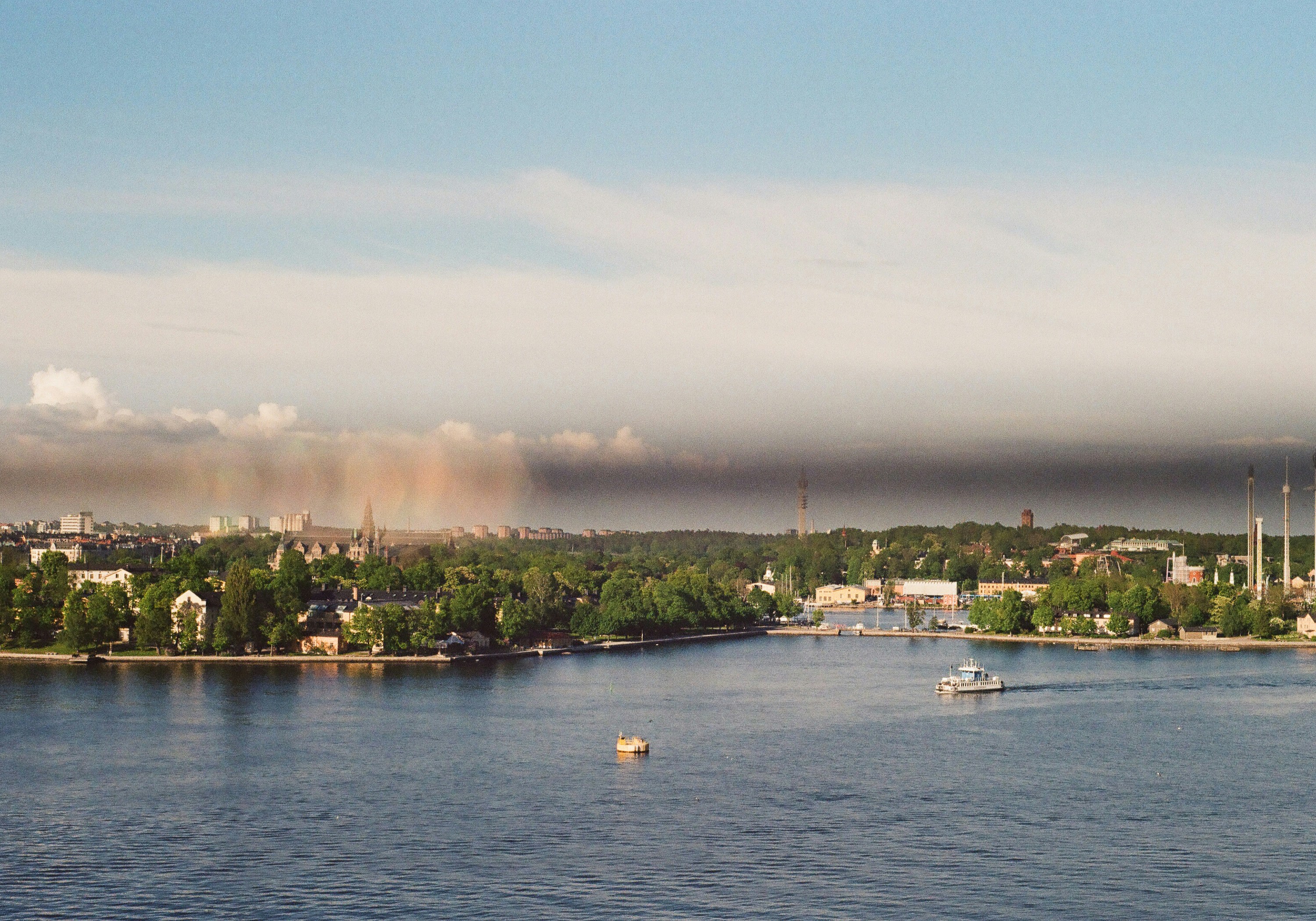 Stadtlandschaft über Wasser mit fernem Regen und schwachem Regenbogen
