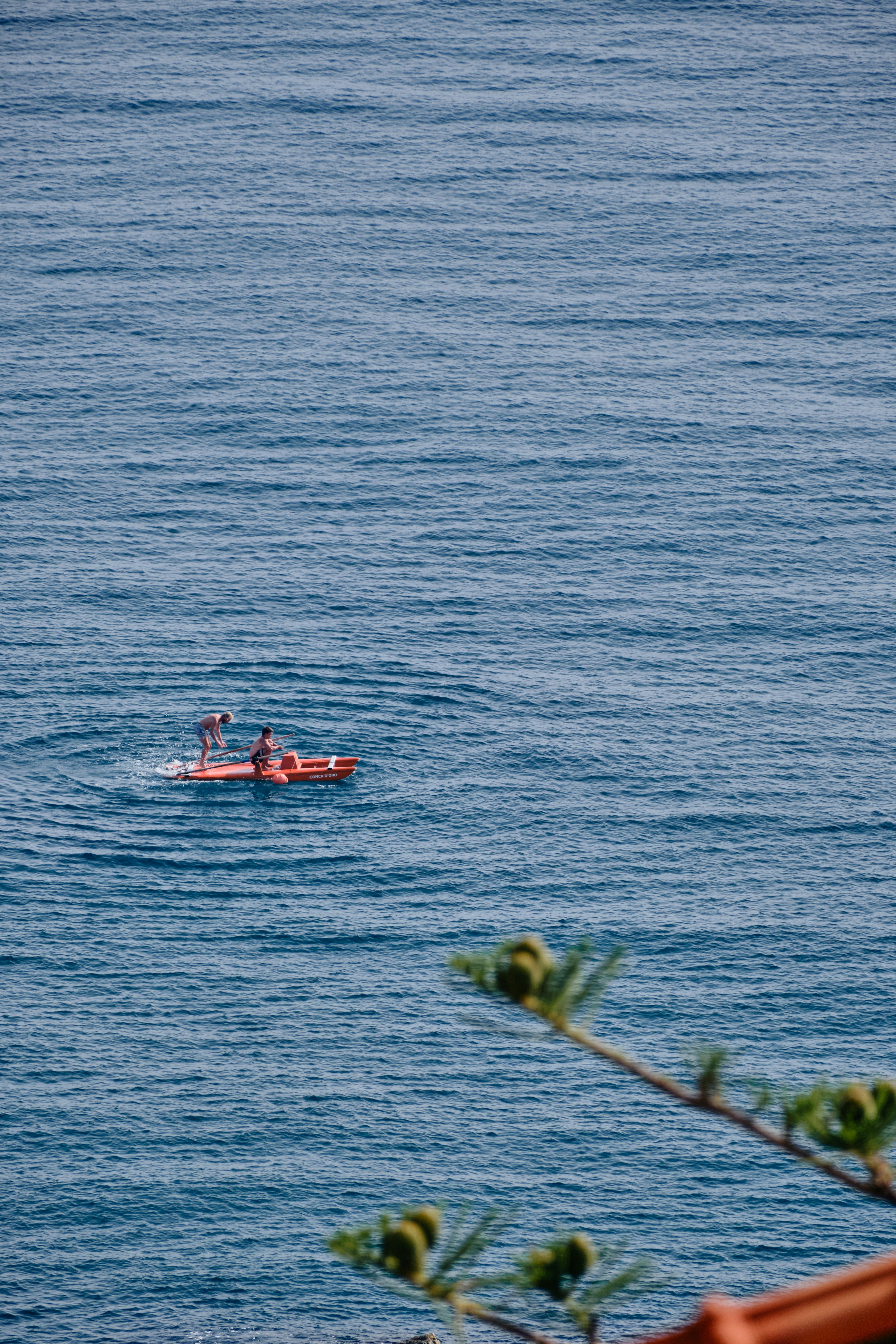 Deux personnes pagaient sur un kayak rouge sur une eau bleue calme.