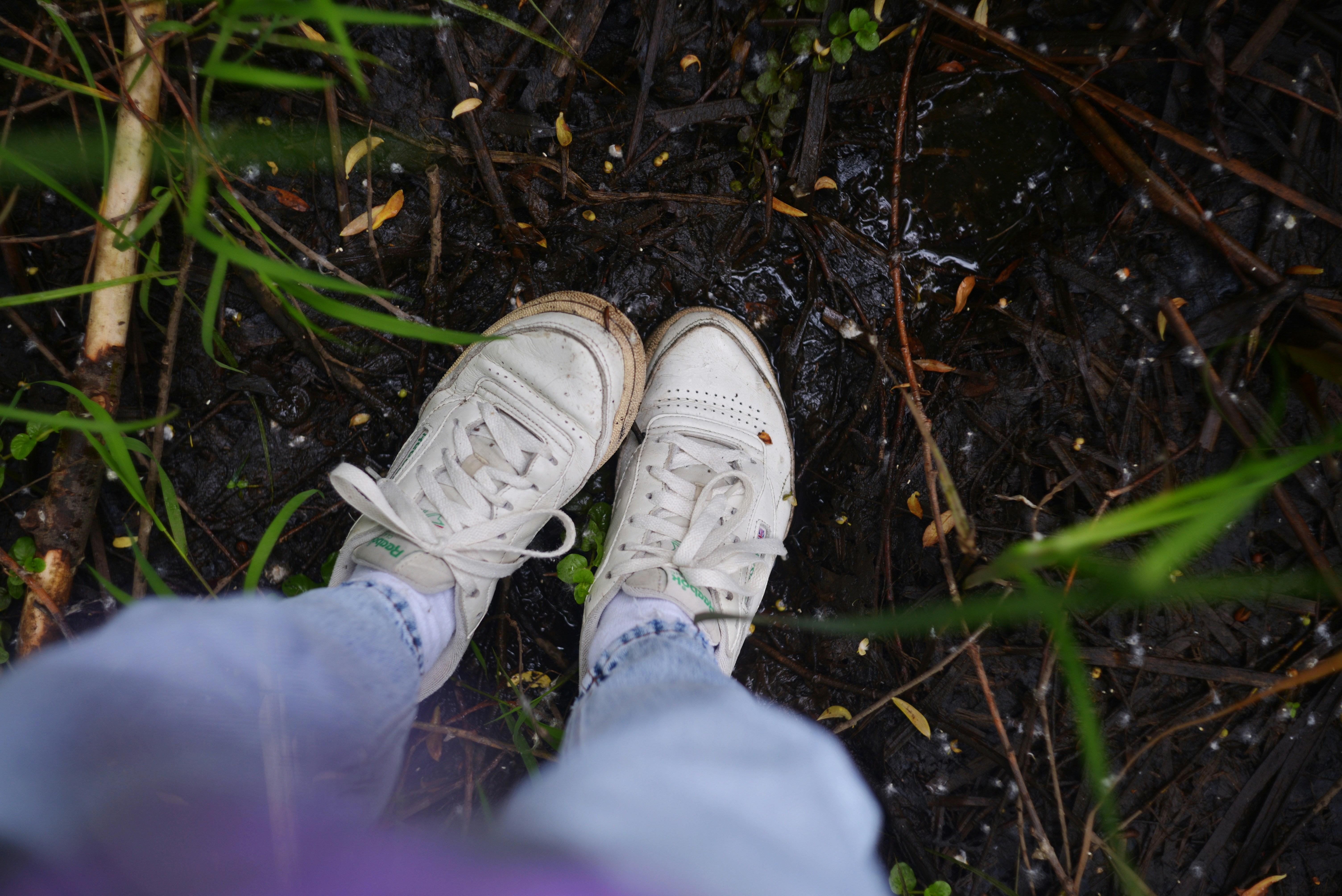 진흙탕 바닥에 흰 운동화를 신은 발, 푸른 잔디.