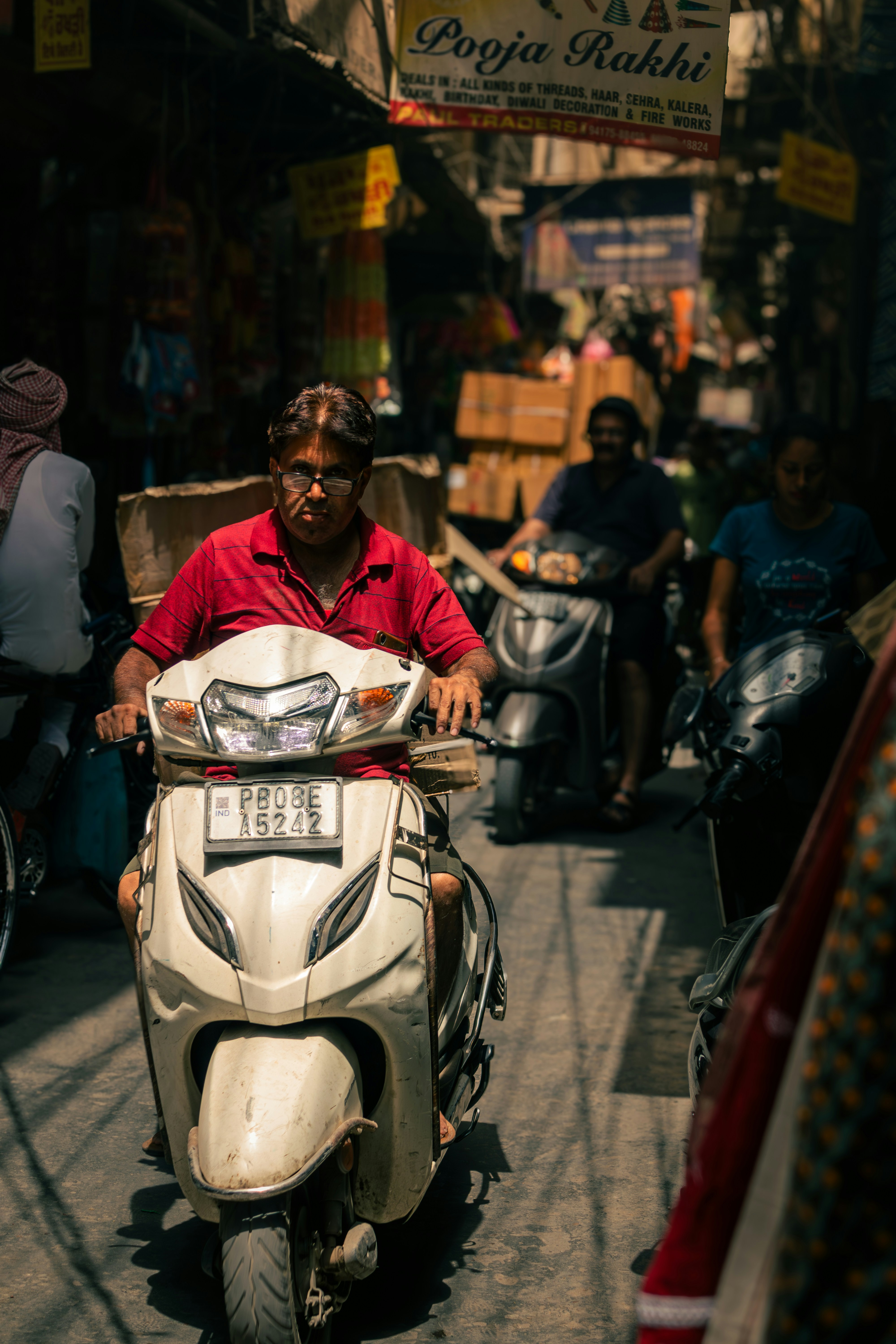 Man rides white scooter through a bustling market lane.
