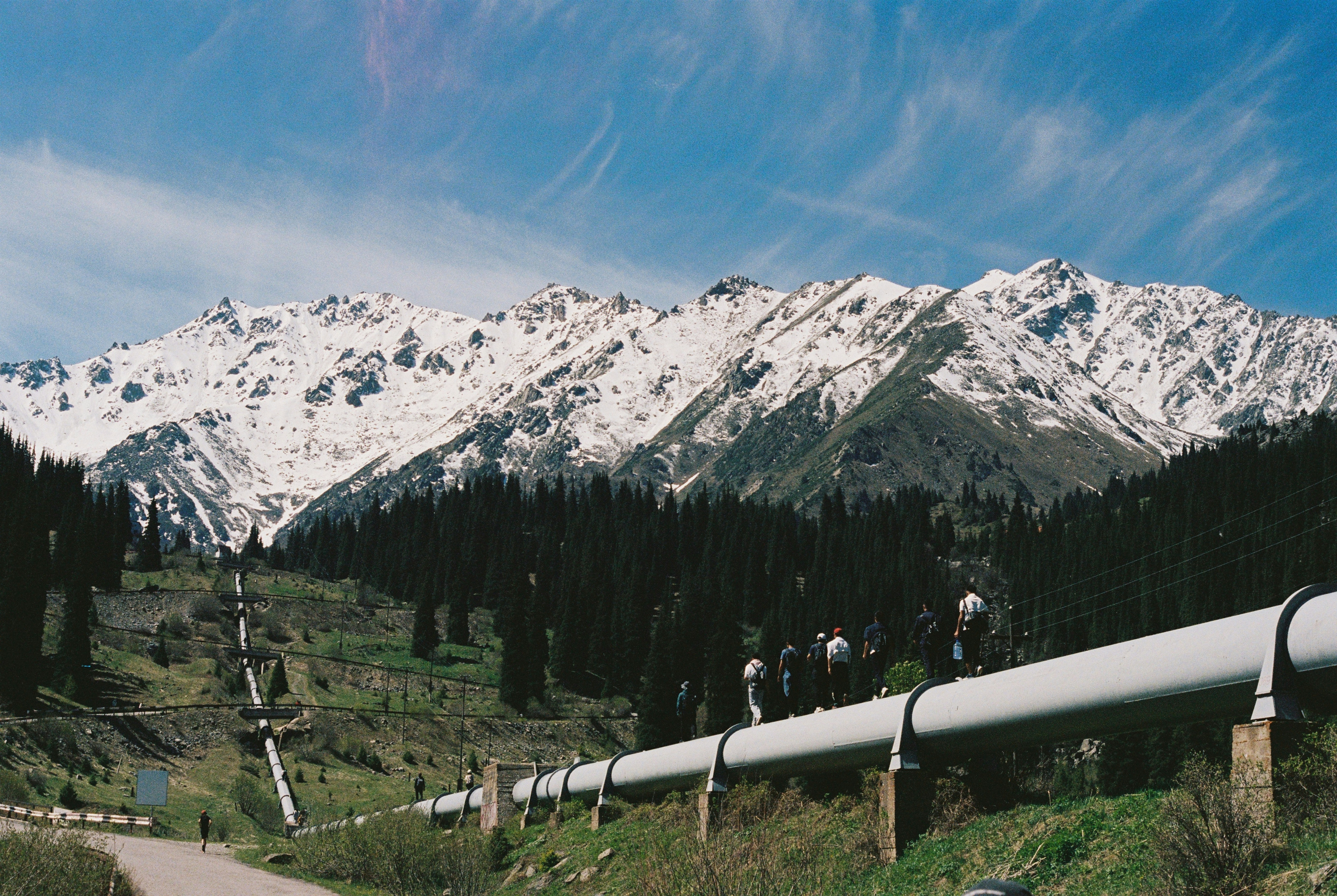 A large pipeline runs through a valley towards snow-capped mountains.