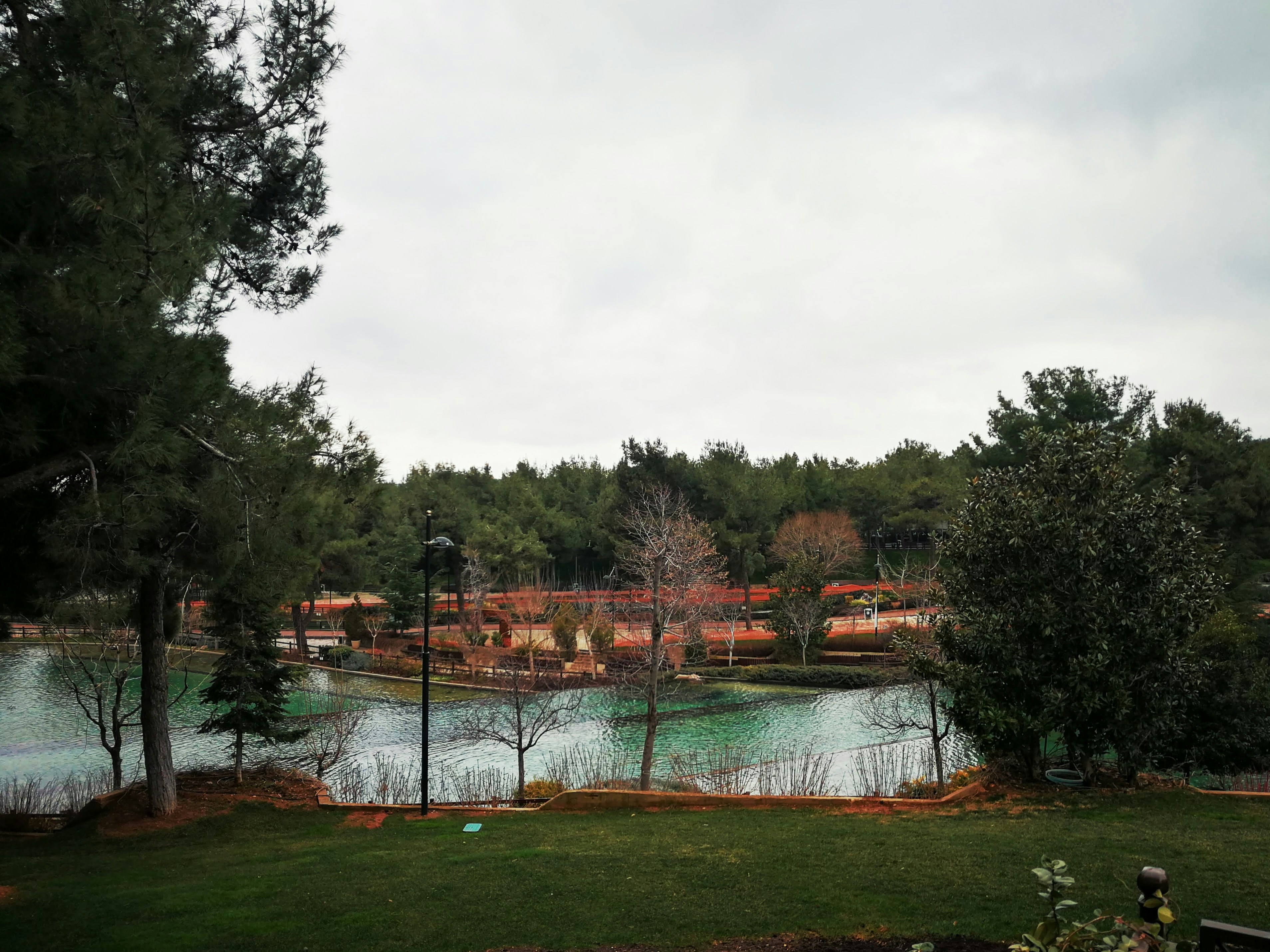 Lake surrounded by trees and buildings on a cloudy day.