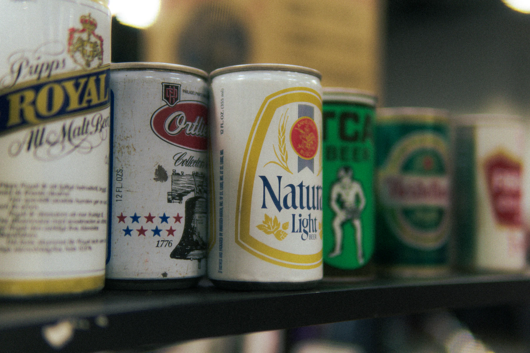Close-up of a row of vintage steel beer cans standing side by side on a dark shelf