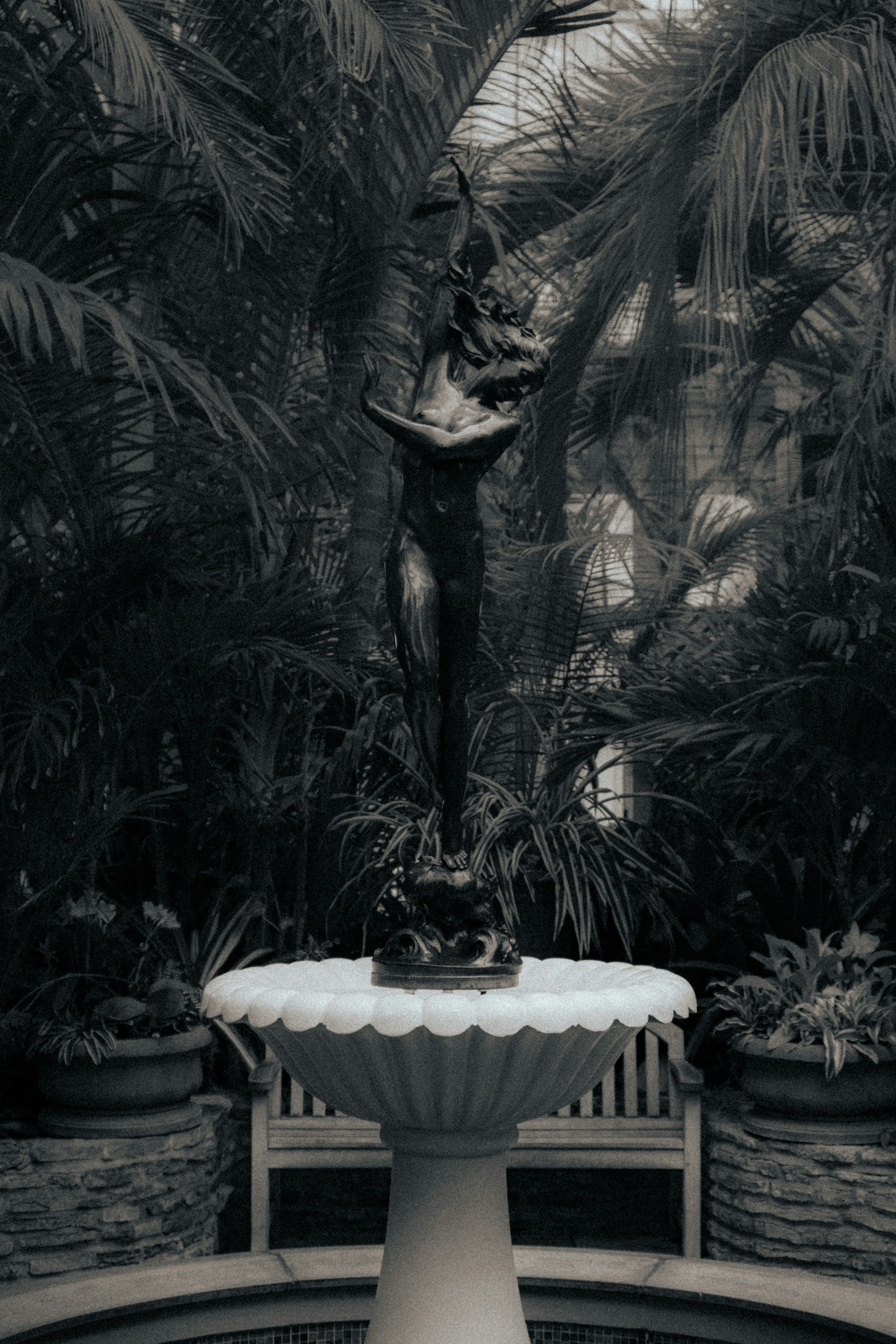 Statue ornée sur une fontaine entourée d’un feuillage tropical sombre.